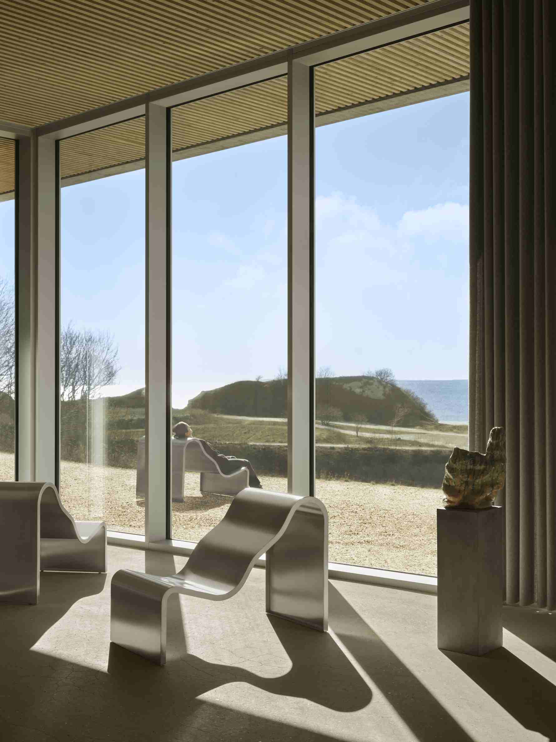 Helle Innenaufnahme mit Muuto Dream Bench Outdoor Bank und Blick auf Dünenlandschaft.