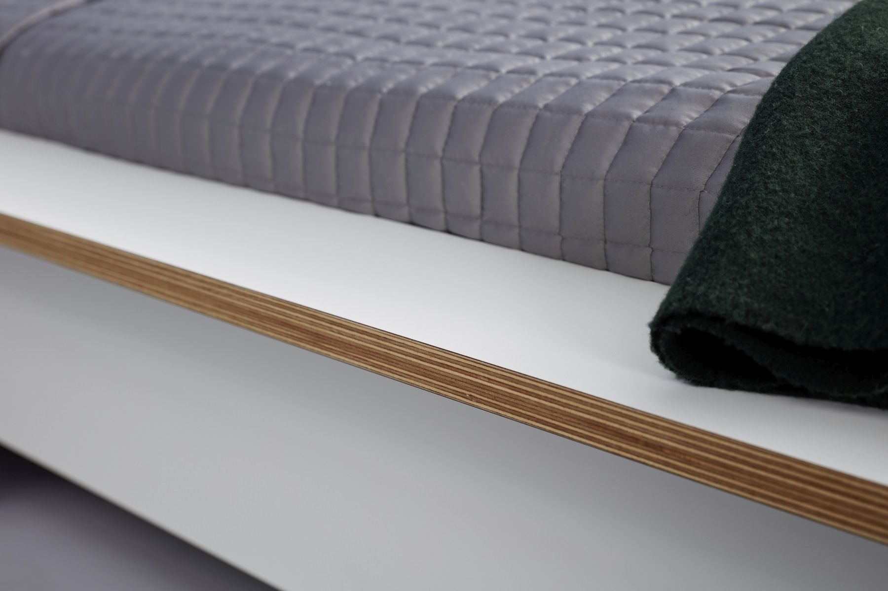 Detailaufnahme: Plane Doppelbett von Müller Möbelwerkstätten mit grauer Tagesdecke und grüner Wolldecke.