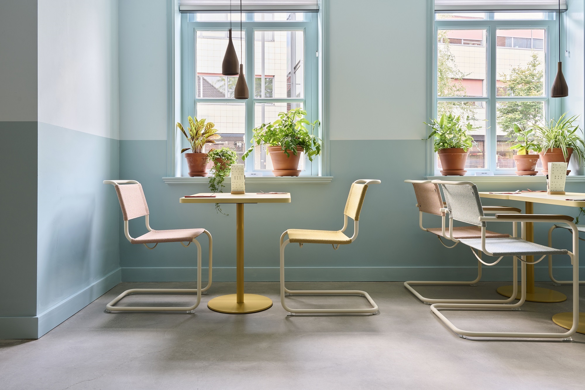 Innenaufnahme mit Thonet S 34 Freischwinger Stühlen in verschiedenen Farben an gelben Tischen vor hellblauen Wänden.