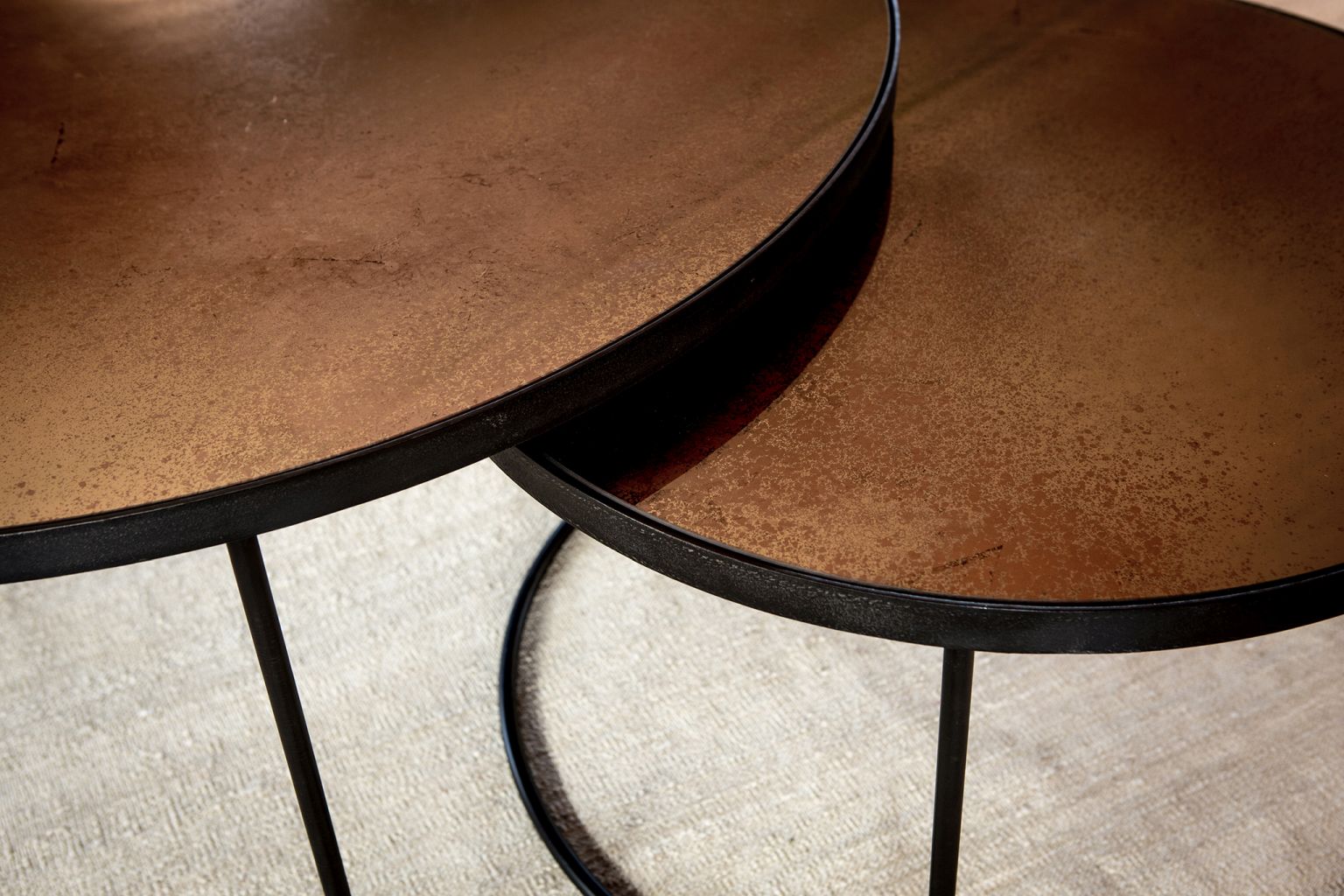 Detailaufnahme: Ethnicraft Couchtisch 2er Set bronze, runde Tischplatten, schwarzes Metallgestell.