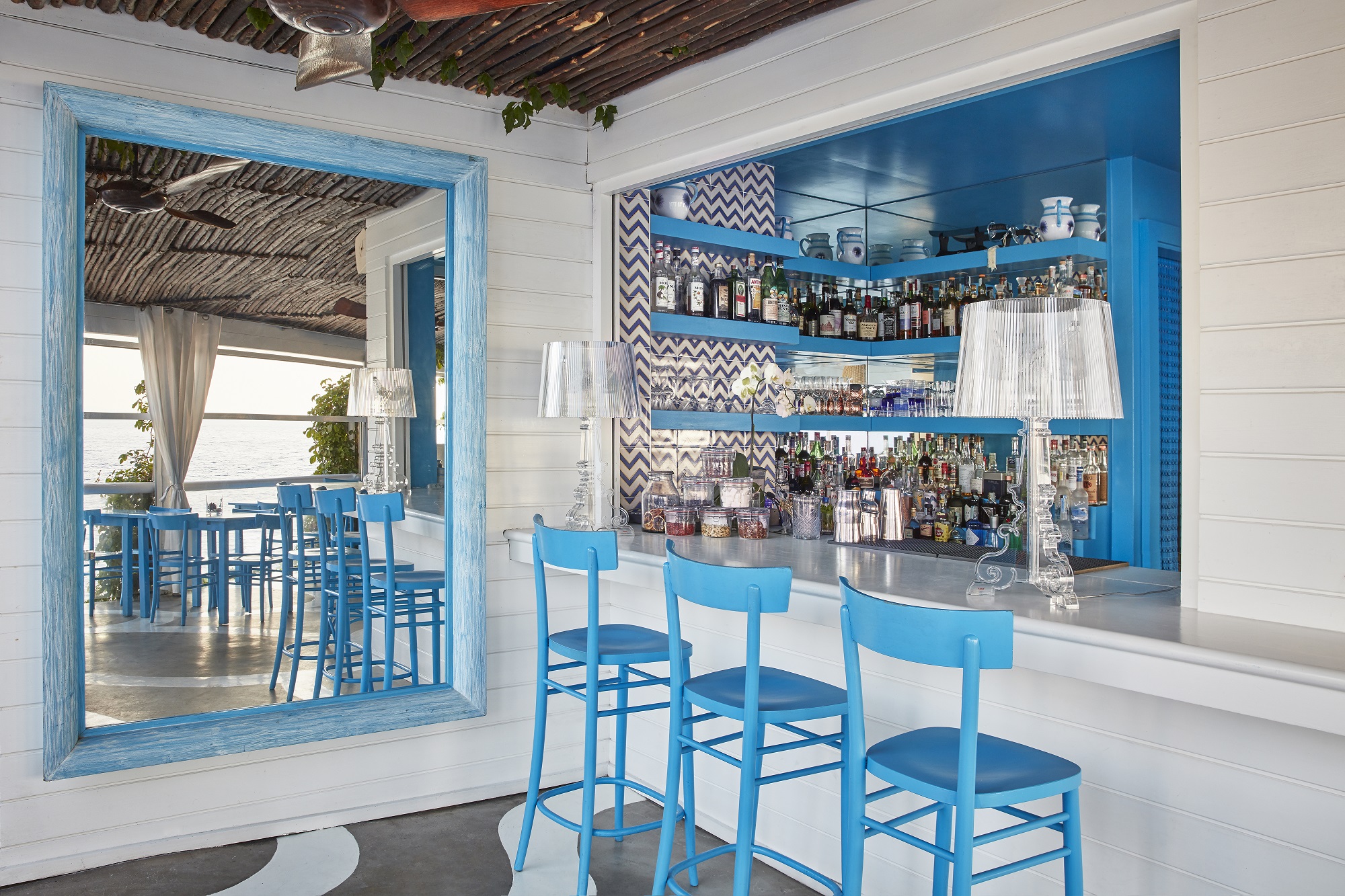 Nahaufnahme einer klaren, dimmbaren Bourgie Tischleuchte von Kartell auf einer Bar mit blauen Stühlen.