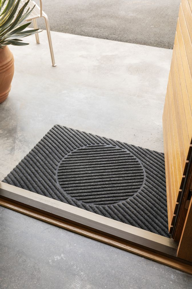 Graue Måne Fußmatte von Heymat vor einer Holztür, mit geripptem Kreisdesign für den Innenbereich.