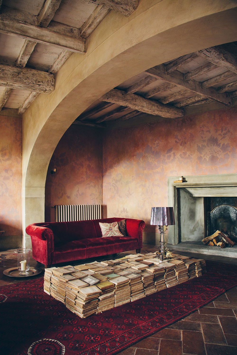Bourgie Tischleuchte von Kartell in einem Wohnzimmer mit rotem Sofa und Bücher-Couchtisch.
