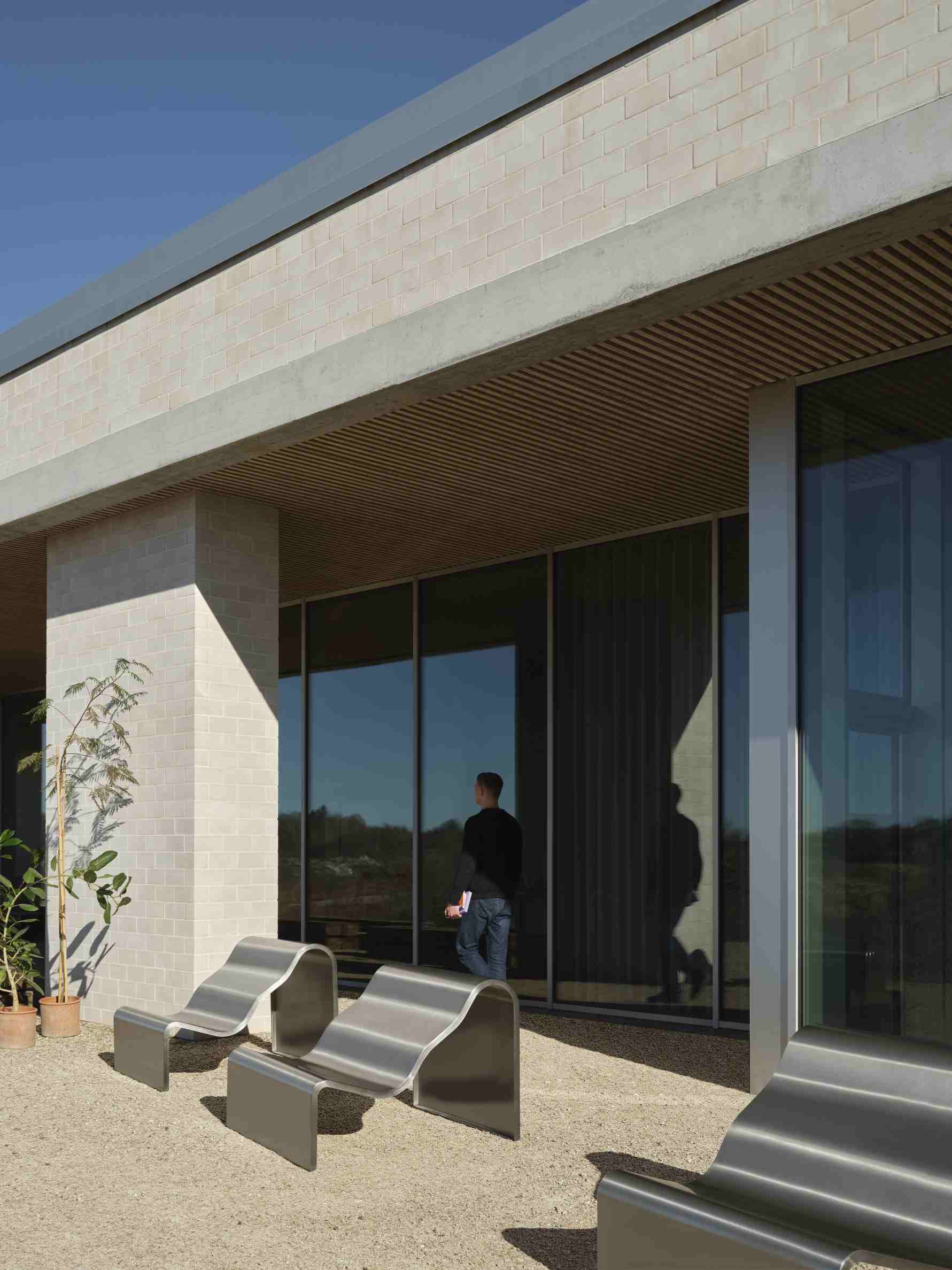Muuto Dream Bench Indoor/Outdoor Bank aus gebogenem Metall vor modernem Gebäude mit Glasfassade.