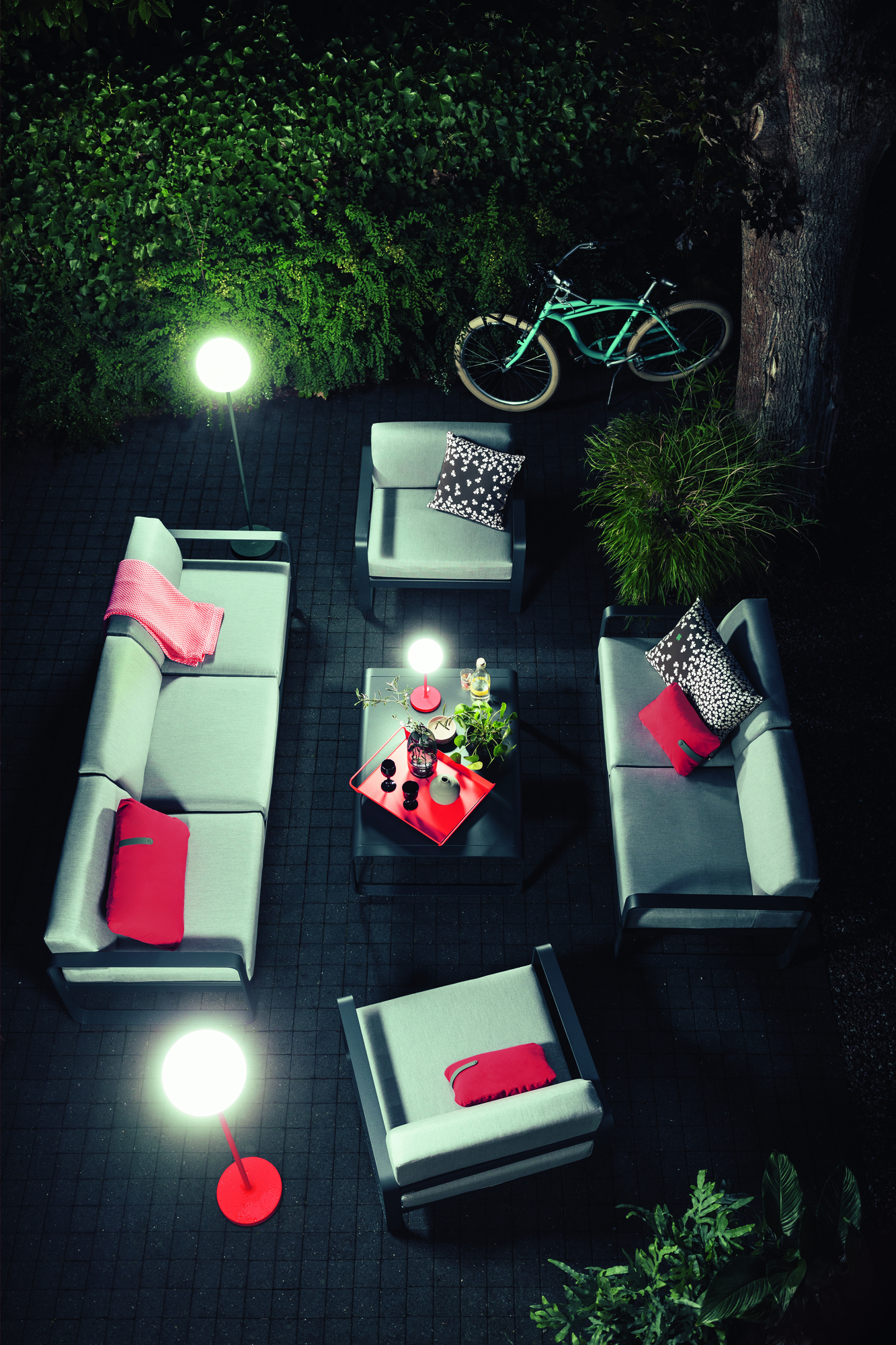 Anthrazitfarbene Mooon! Stehleuchte von Fermob beleuchtet eine moderne Outdoor-Lounge mit Gartenmöbeln und Dekoration.
