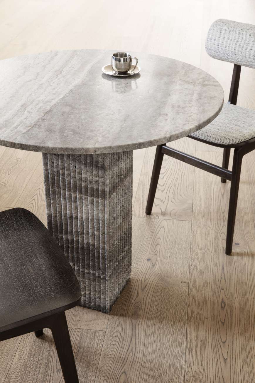 Nahaufnahme des NORR11 Totem Chair Stuhls mit grauem Steintisch und dunklen Holzstühlen auf Holzboden.