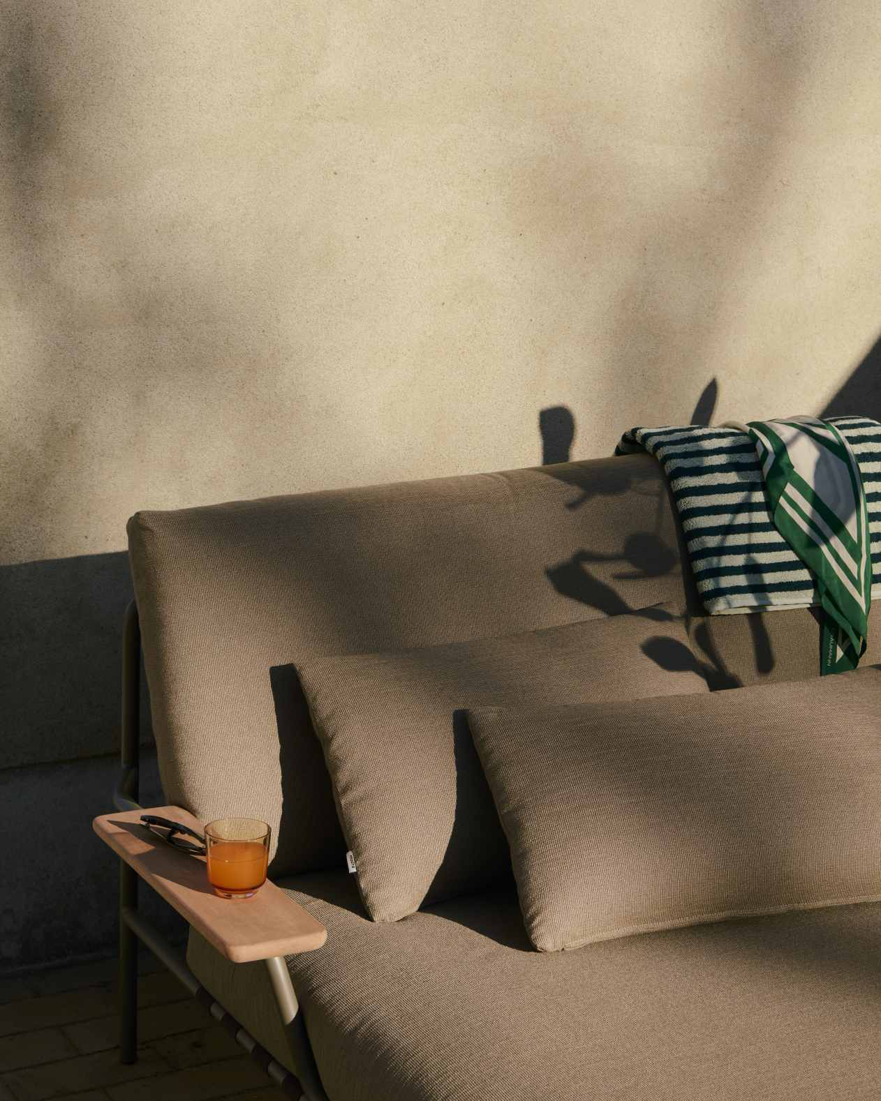 Muuto Settle Lounge Bed Outdoor Liege mit Kissen und Getränk im Garten.