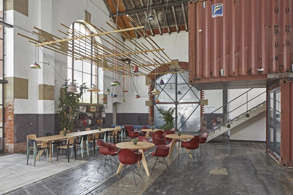Innenaufnahme mit mehreren Gueridon Tischen von Vitra, runden Holztischplatten und roten Stühlen in einem industriellen Raum.