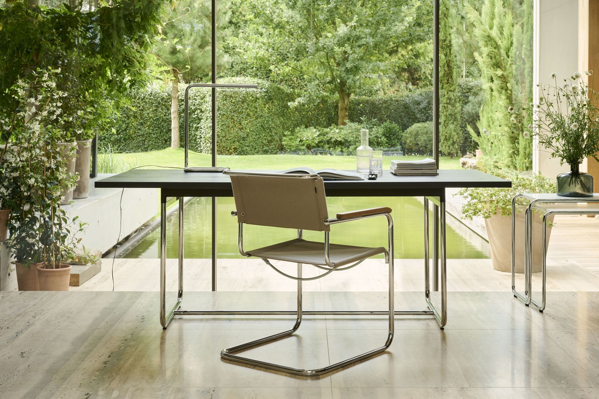 Thonet S 34 Freischwinger Stuhl mit Stoffbezug und Holzarmlehnen am Schreibtisch vor Fenster mit Gartenblick.