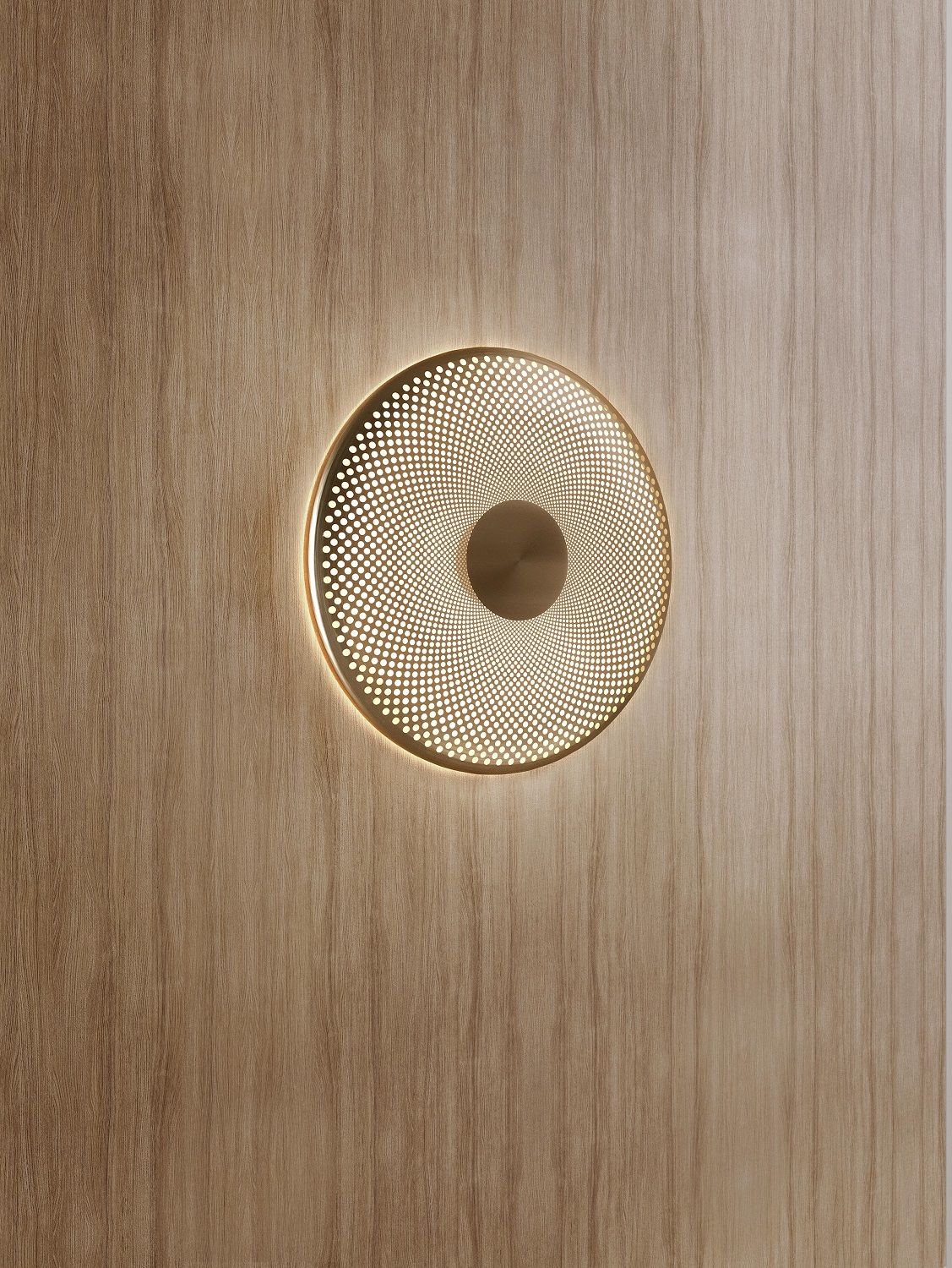 Glint Wandleuchte von Northern, runde goldene Wandlampe mit dekorativem Lichtmuster an einer Holzwand.