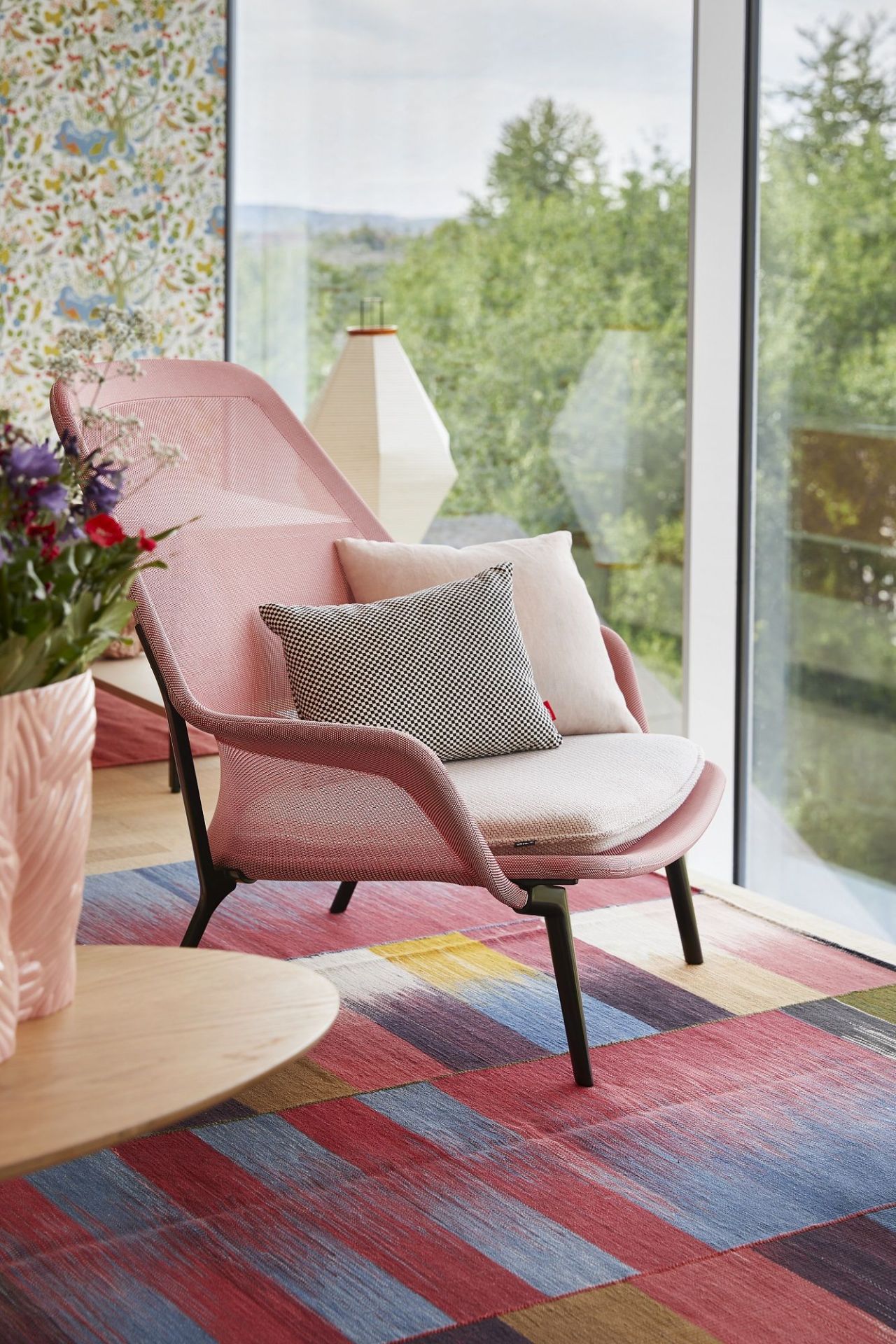 Rosa Vitra Slow Chair Sessel mit Kissen vor Fenster und farbenfrohem Teppich für entspanntes Wohnen.
