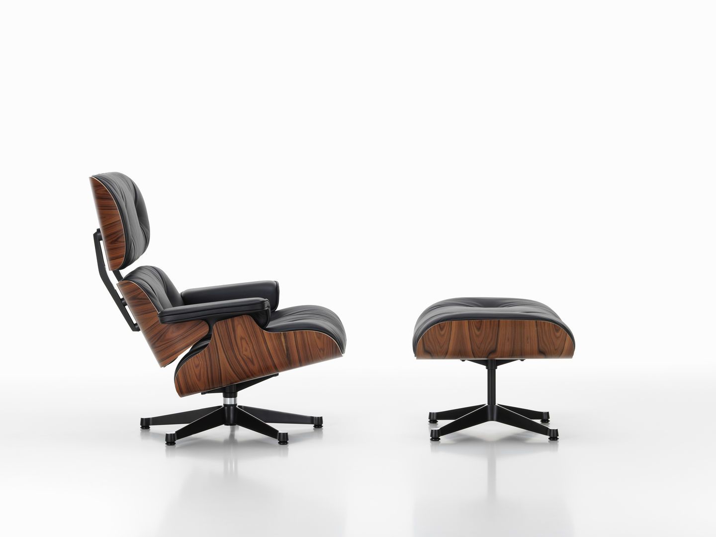 Eames Lounge Chair mit Ottoman in schwarzem Leder und dunklem Holzfurnier, seitliche Ansicht.
