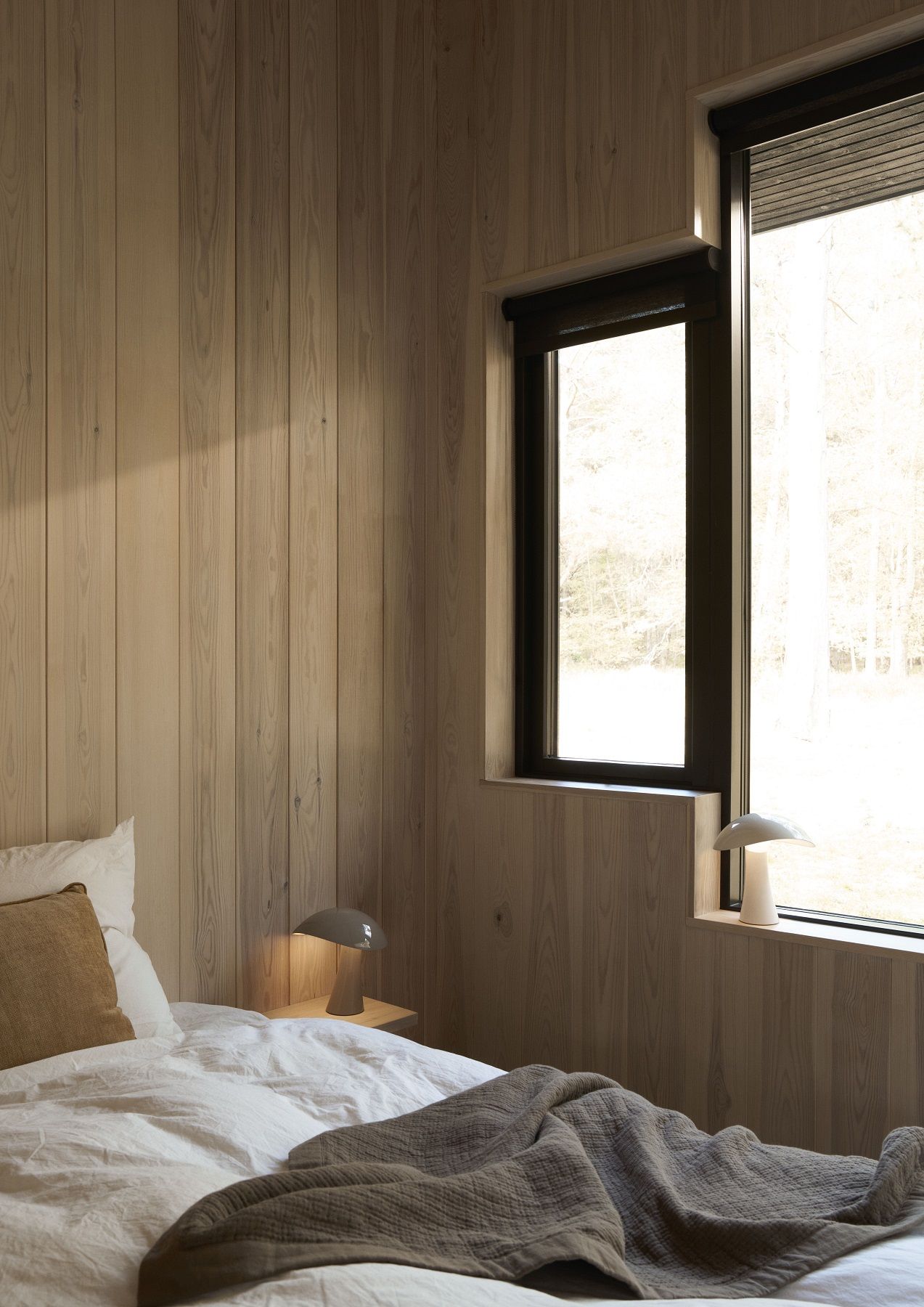 Rumee Akkuleuchte von Louis Poulsen auf Nachttisch im Schlafzimmer mit Holzwand und Fenster.