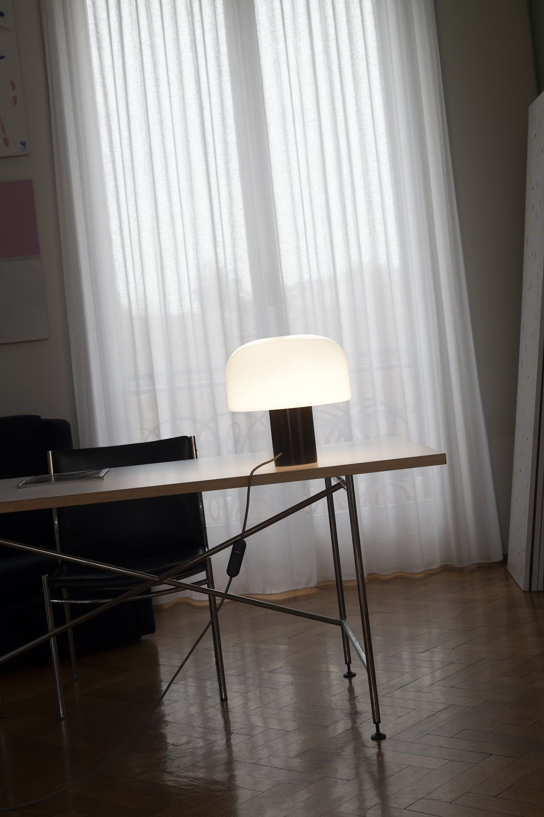 Bellhop Tischleuchte von Flos: Moderne Lampe mit Glasschirm auf einem Schreibtisch vor einem Fenster.