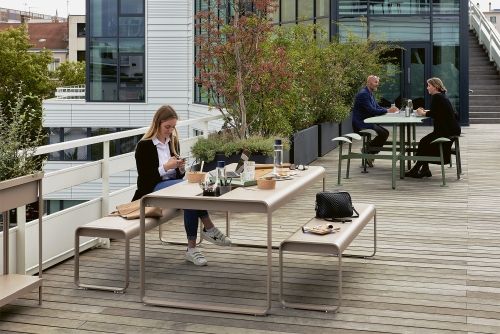 Bolder 3-Sitzer Tisch mit Sitzflächen von Fermob im Außenbereich, Menschen sitzen und arbeiten.
