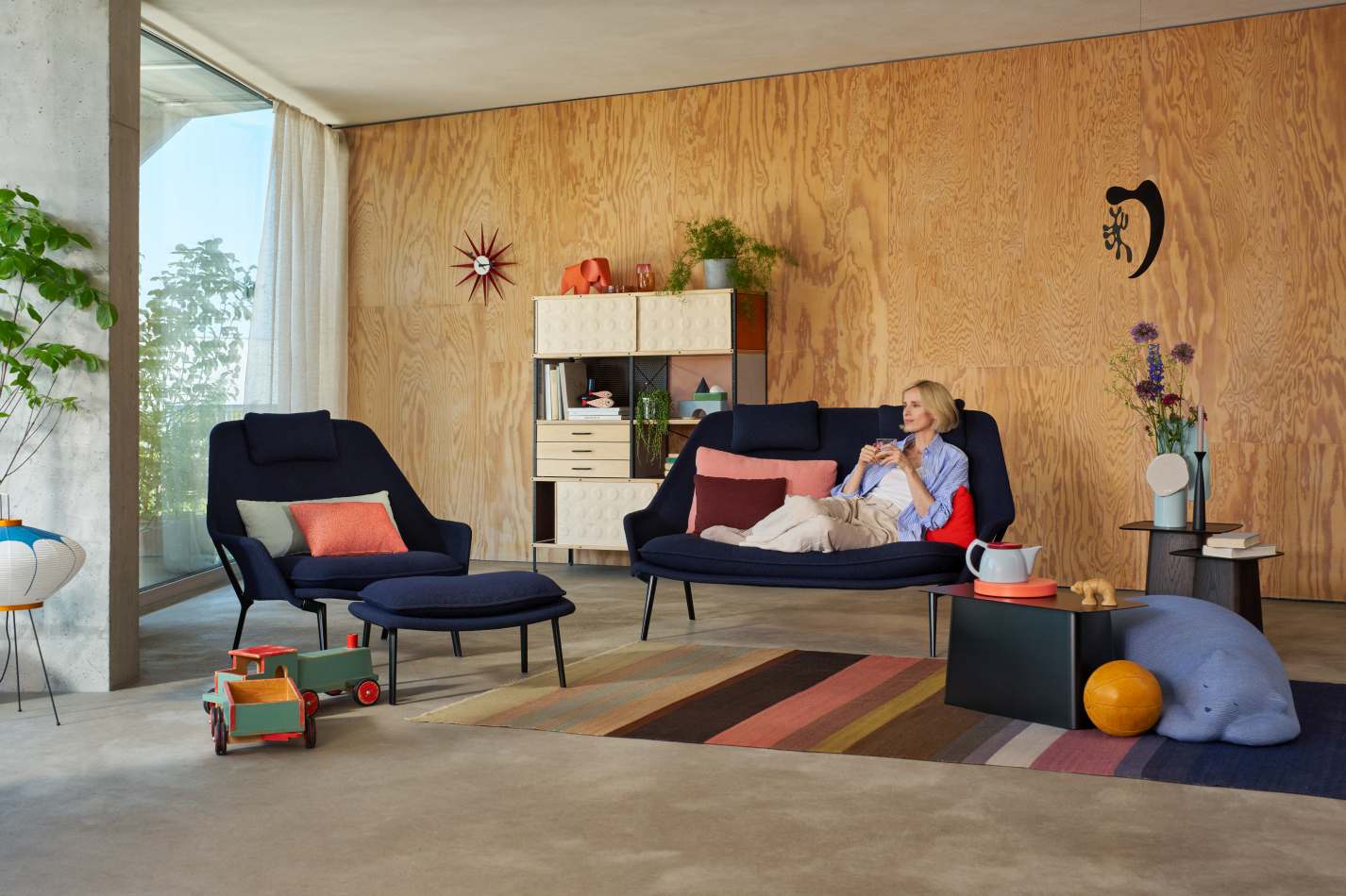 Wohnzimmer mit Vitra Slow Sofa und Sessel in blauem Stoff, Frau entspannt auf dem Sofa.
