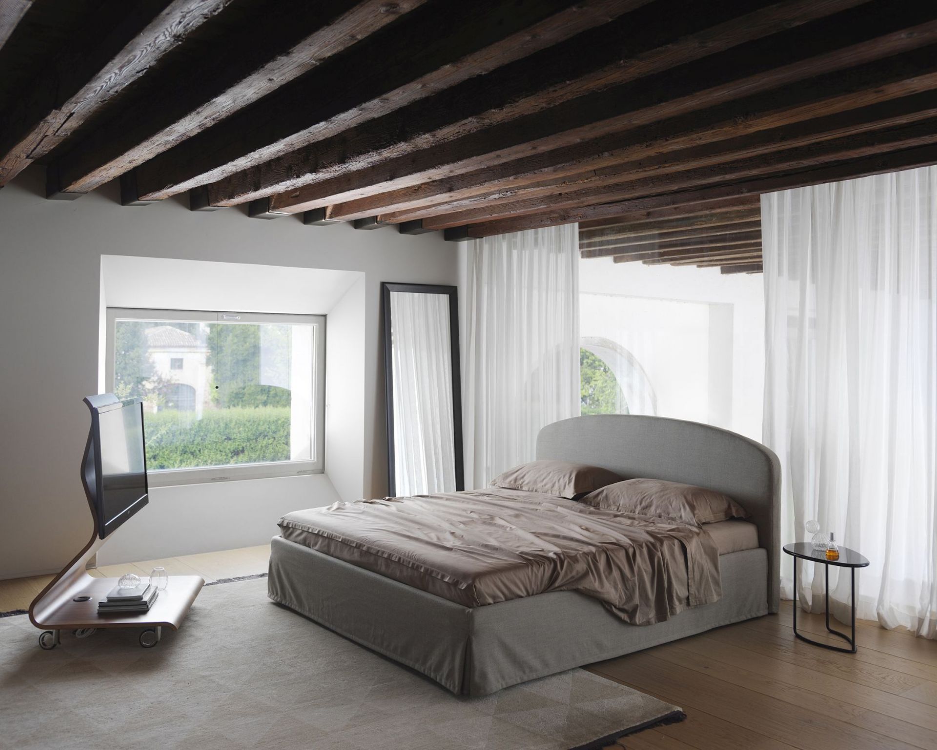 Schlafzimmer Interieur mit Yume Black Spiegel von Casamania Horm, Bett, Fenster und Holzbalkendecke.