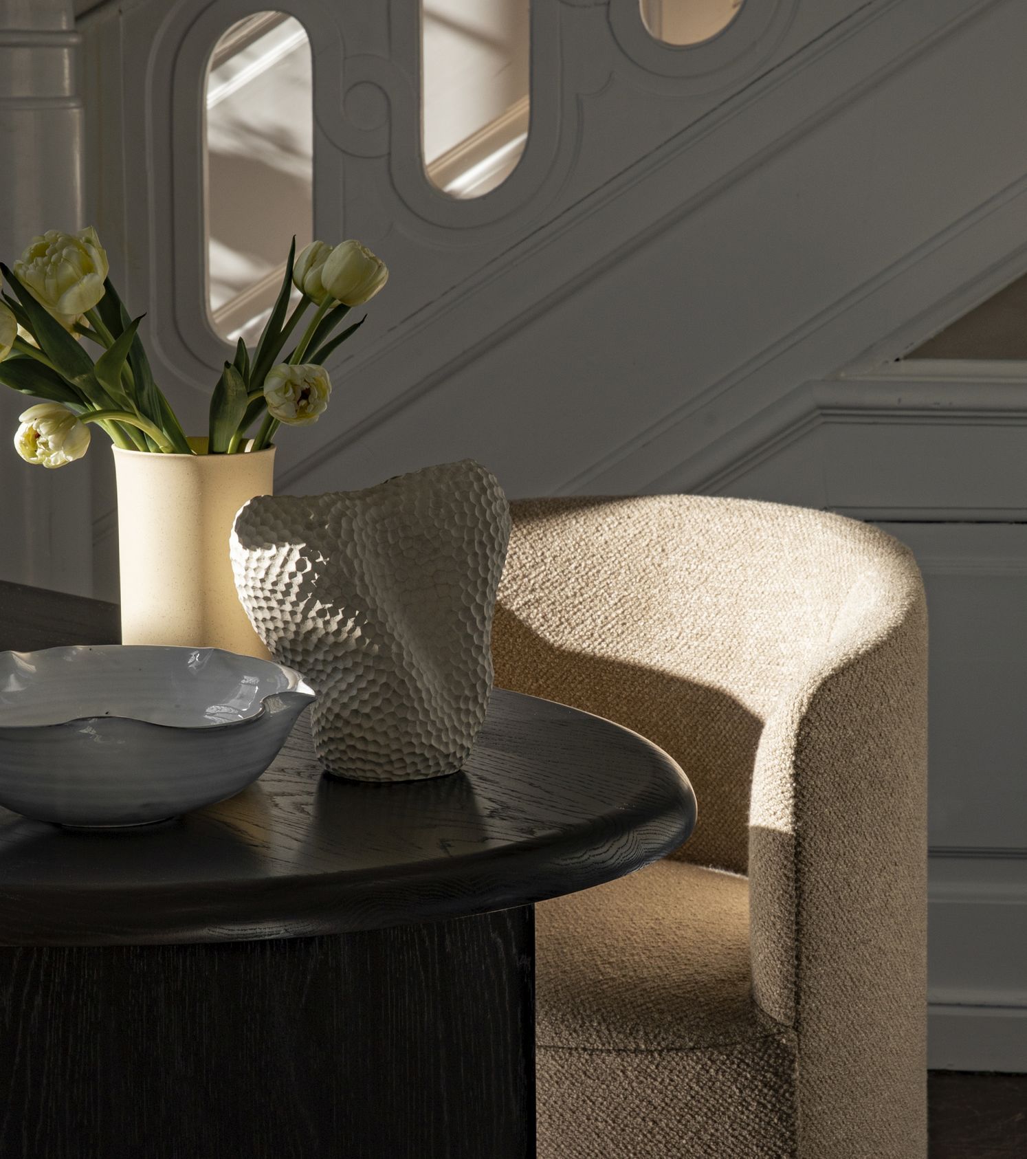 Beiger Tearoom Lounge Chair Sessel von Audo Copenhagen neben dunklem Holztisch mit Deko.