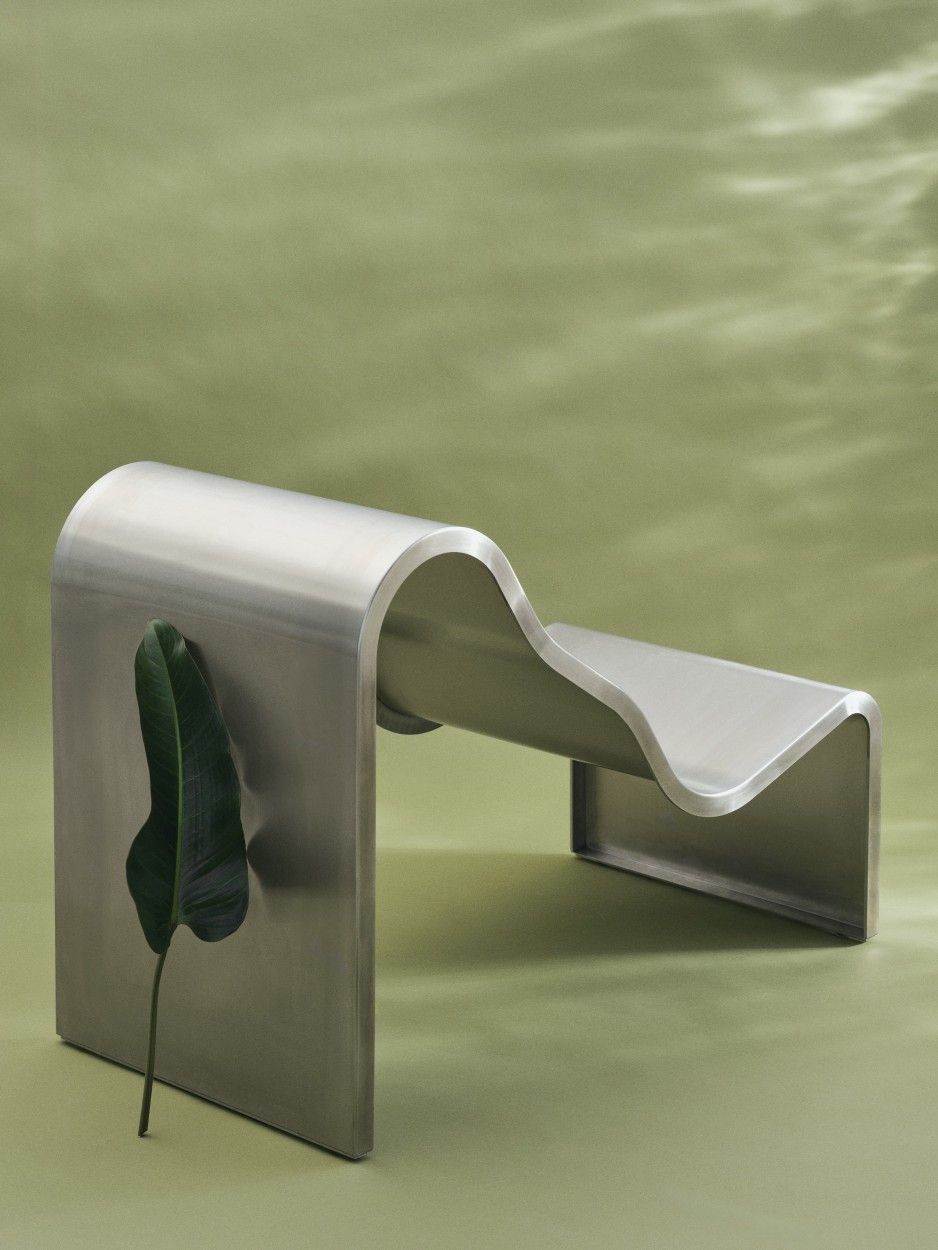 Muuto Dream Bench: Moderne Indoor/Outdoor Bank aus gebogenem Metall mit Blatt auf grünem Hintergrund.