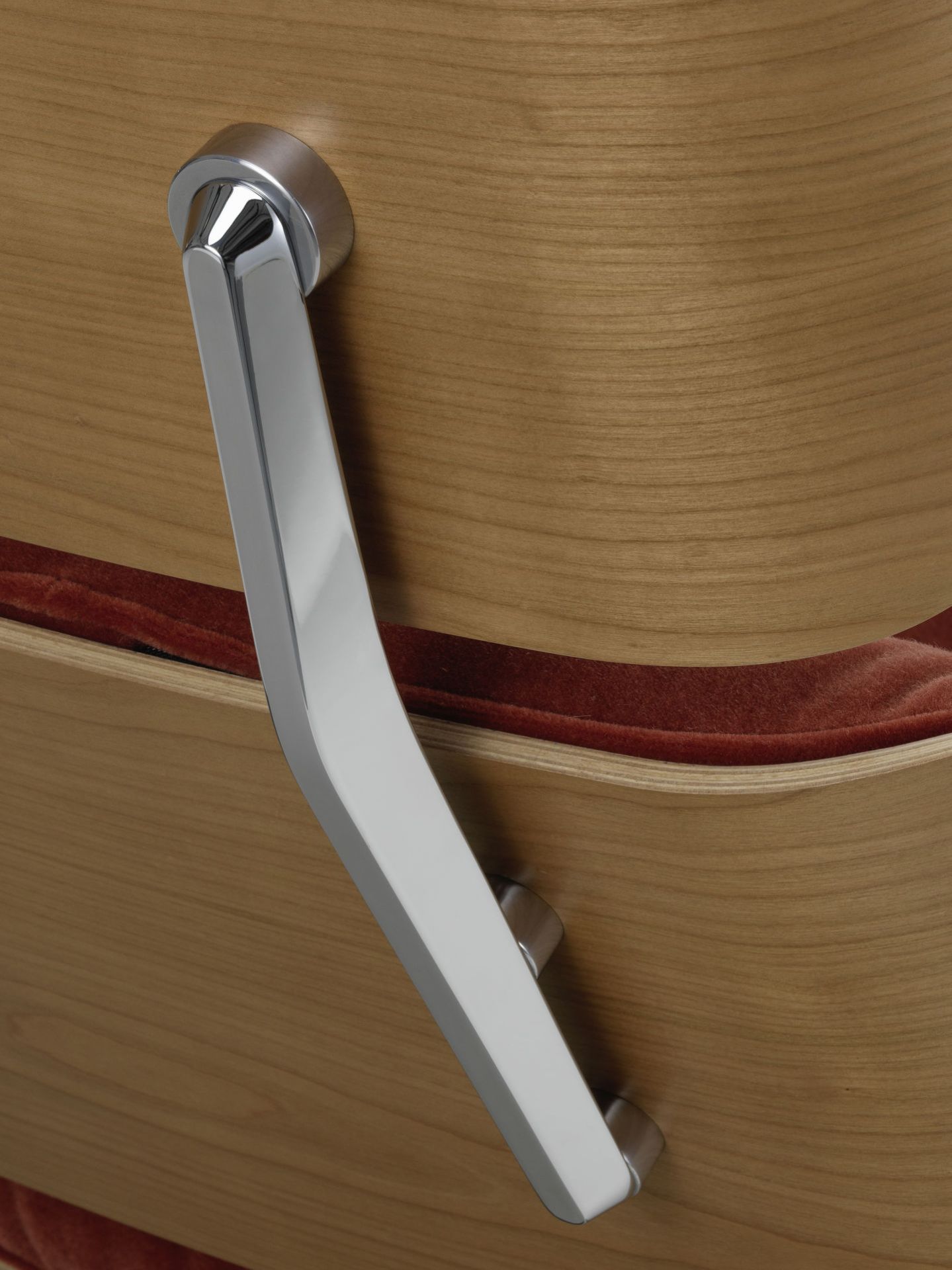 Detailaufnahme: Verchromter Arm des Eames Lounge Chair von Vitra mit Holzschale und rotem Polster.