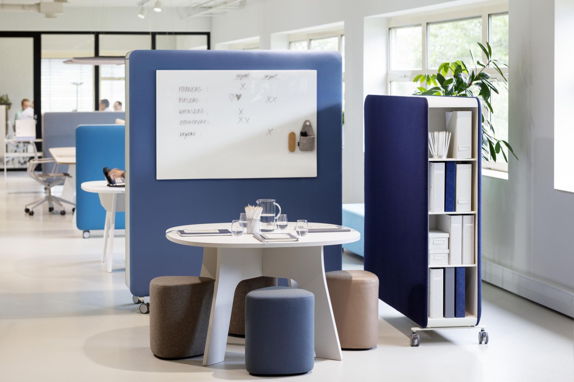 Büro mit Cascando Pillow Space Akustik-Raumteilern in Blau, Whiteboard, Tisch, Hocker und Regal.