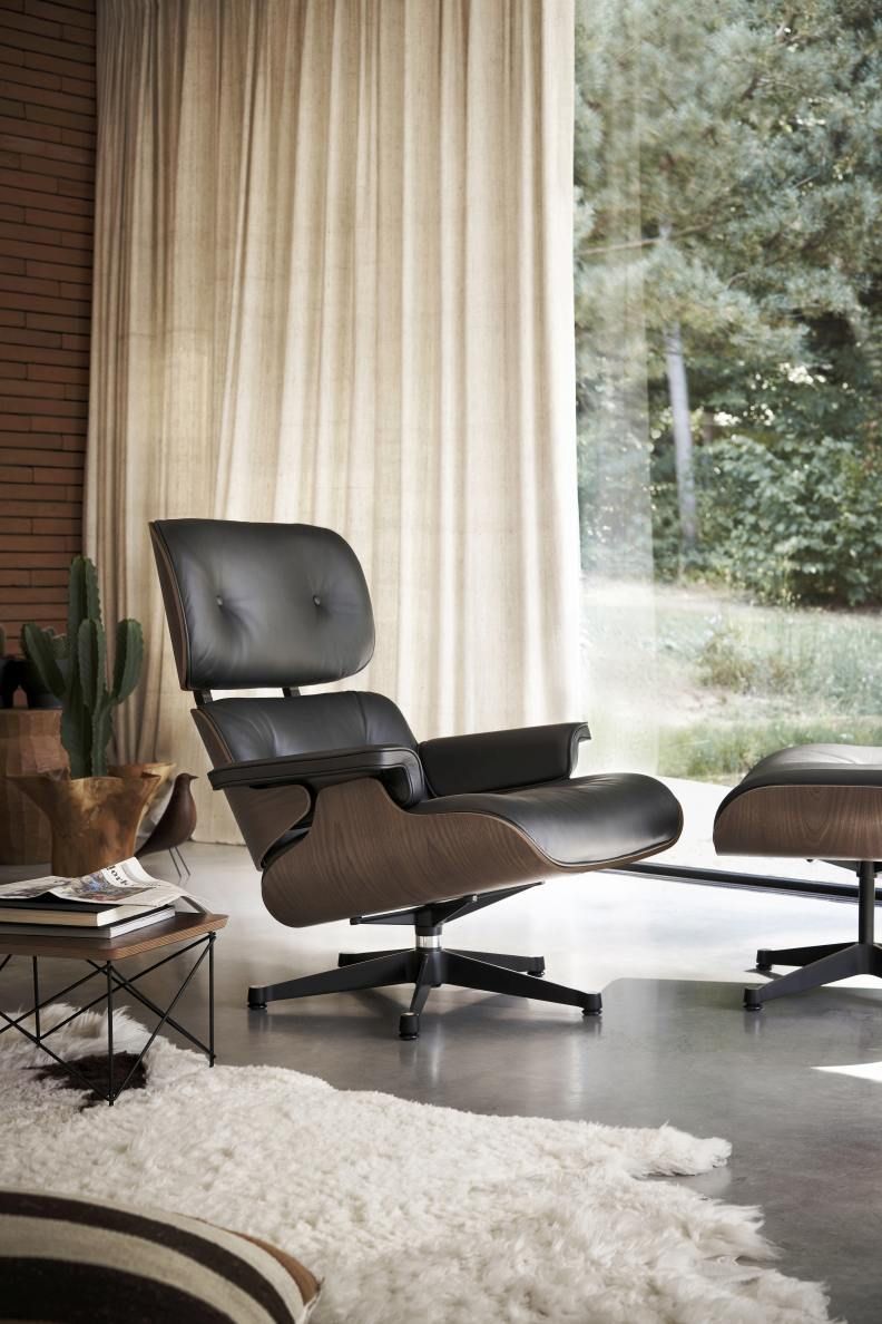 Eames Lounge Chair mit Ottoman in schwarzem Leder und dunklem Holzfurnier vor Fenster.