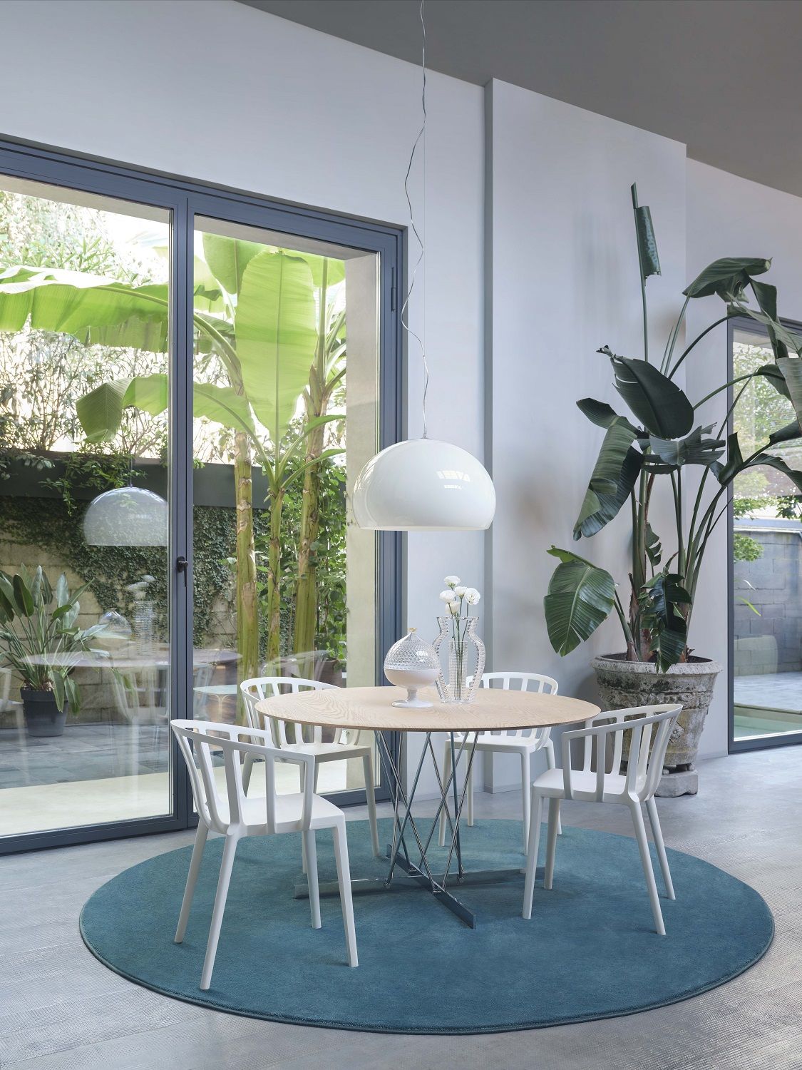 Weiße Fly Pendelleuchte von Kartell über einem Esstisch mit Stühlen und blauem Teppich.