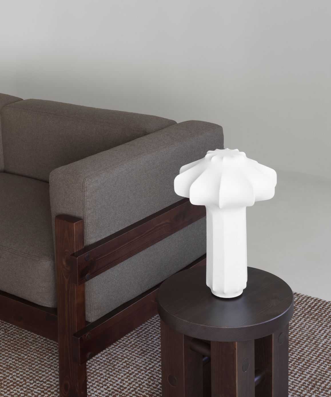 Detailaufnahme vom Normann Copenhagen Kube Sofa in Grau mit dunklem Holzrahmen neben einem Beistelltisch mit Lampe.
