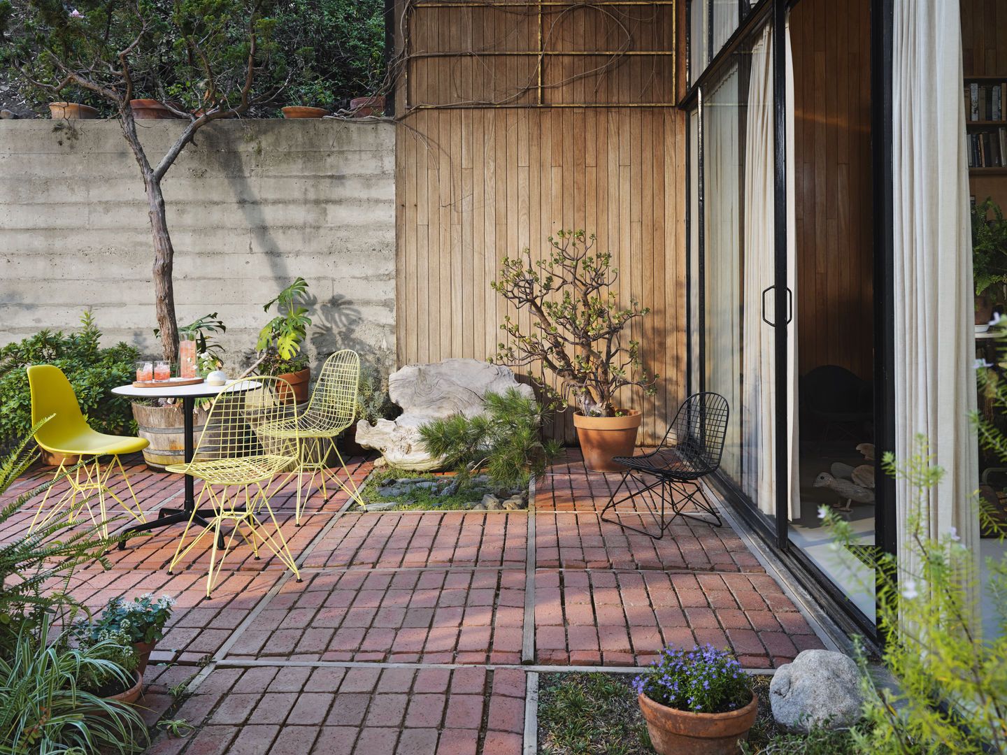 Gelbe und schwarze LKR Wire Chairs von Vitra auf einer Terrasse mit Tisch und Pflanzen.
