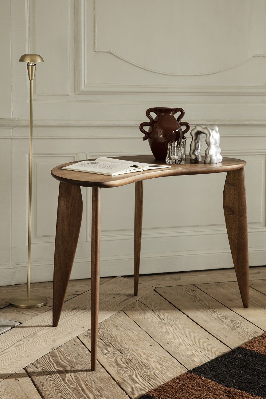Ferm Living Tiny Floor Lamp Stehleuchte neben einem Holztisch mit Deko-Objekten in einem Wohnraum.