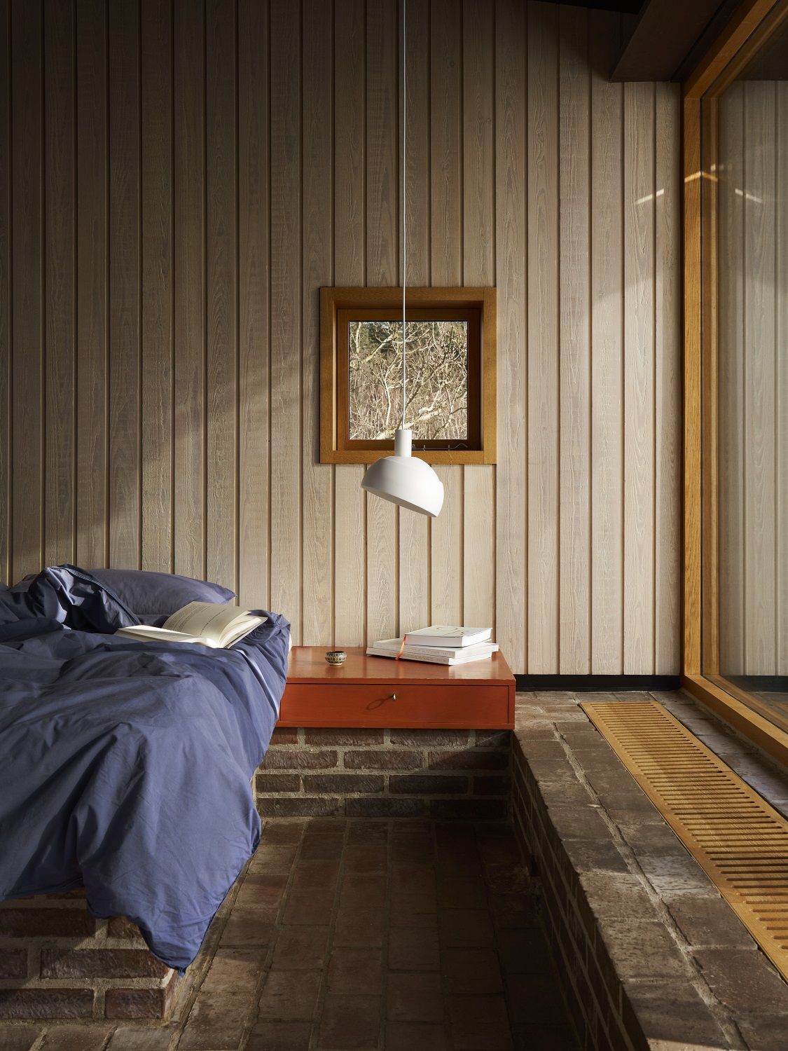 Moderne FJ Elements Pendelleuchte von Louis Poulsen über Nachttisch in stilvollem Schlafzimmer mit Holzwand.