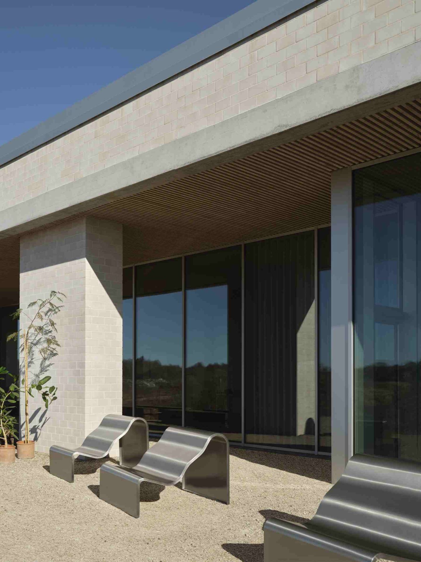 Zwei moderne Muuto Dream Bänke aus Metall stehen im Außenbereich vor einem Gebäude.