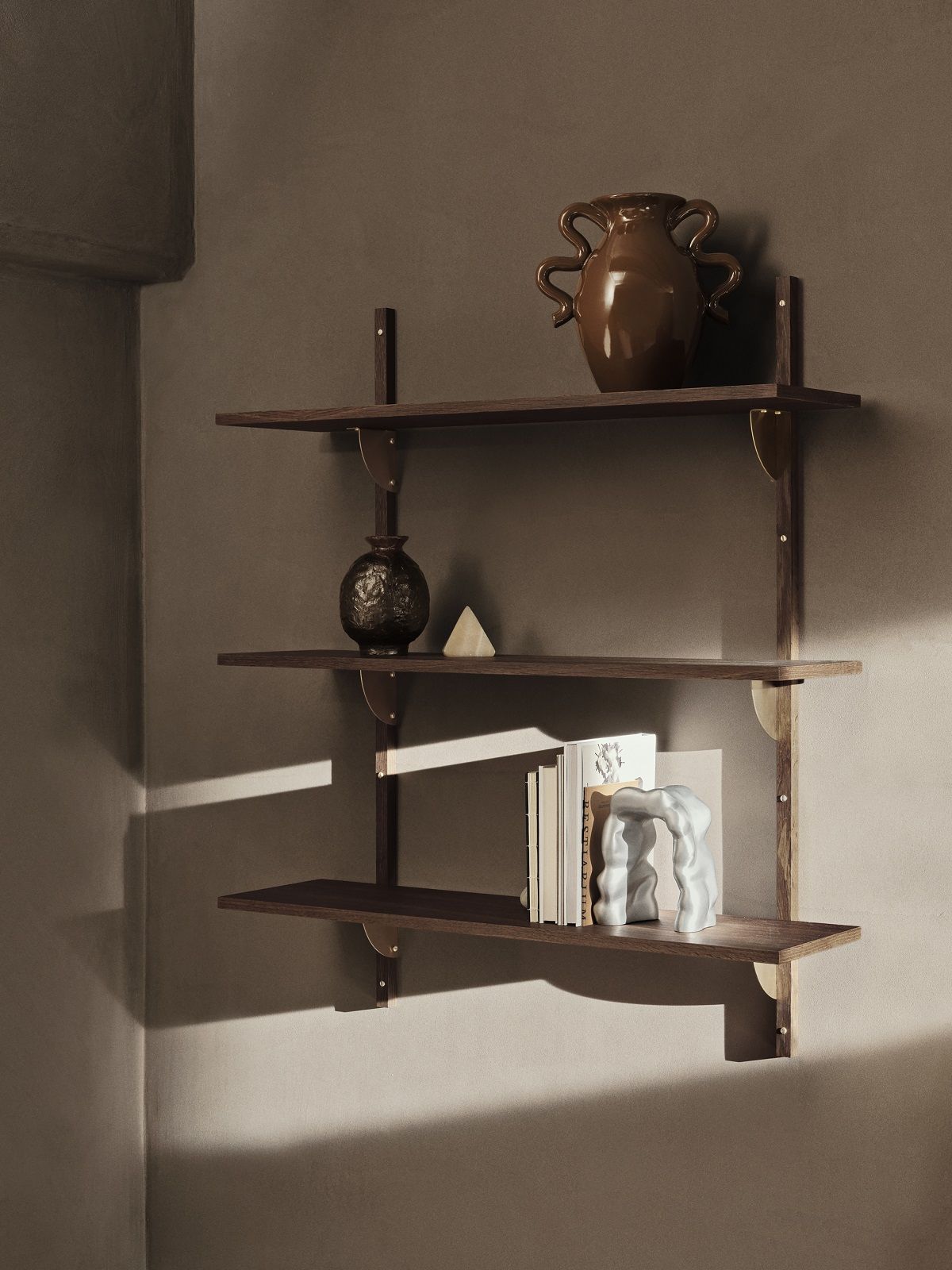 Dunkelbraunes Ferm Living Wandregal mit drei Ebenen, dekoriert mit Vasen und Büchern.