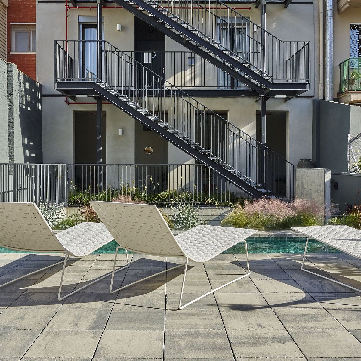 Drei Trenza Outdoor Liegen von Andreu World am Pool, modernes Design mit weißem Gestell.