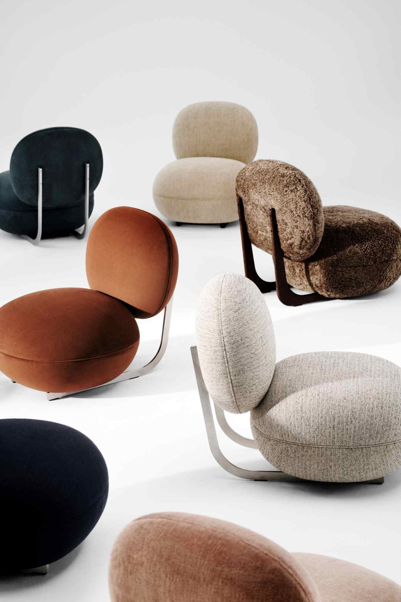Mehrere Copper Lounge Sessel von NORR11 in verschiedenen Farben und Stoffen mit Holz- und Metallgestell.