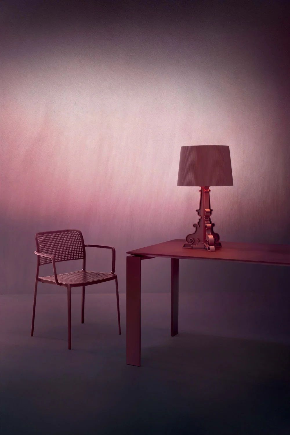 Bourgie Tischleuchte von Kartell in mattem Rot auf einem Tisch neben einem Stuhl.