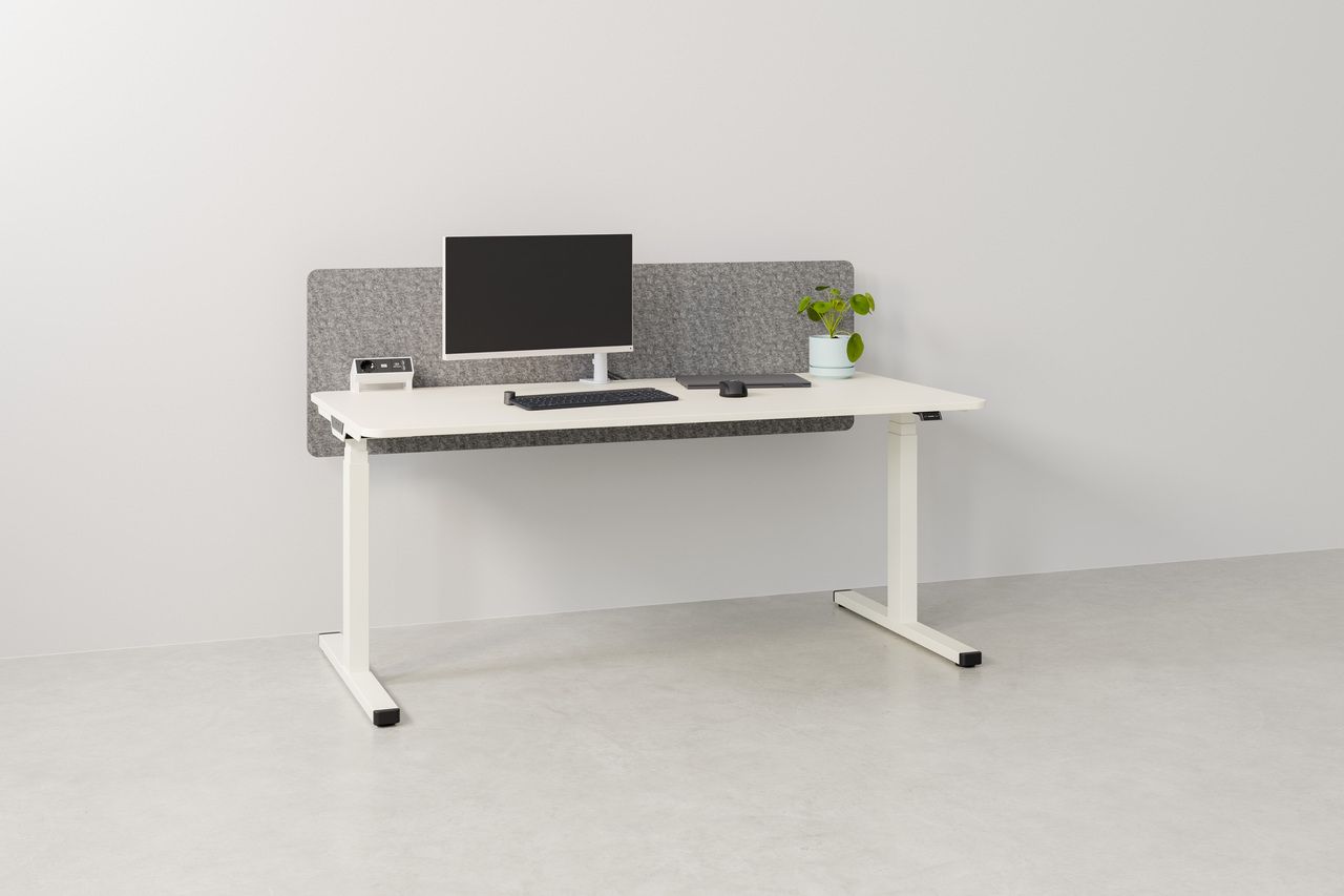 Weißer Palmberg PiD Sitz-Stehtisch mit Monitor, Tastatur, Maus und Pflanze vor grauer Akustikwand.
