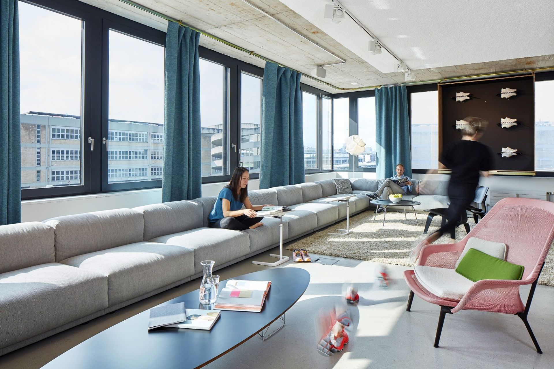 Heller, moderner Büroraum mit großem Sofa und einem pinken Vitra Slow Chair Sessel im Vordergrund.