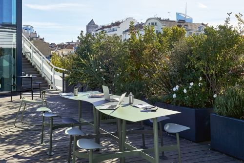Bolder 3-Sitzer Outdoor Tisch mit Sitzflächen von Fermob auf einer Dachterrasse mit Laptops.