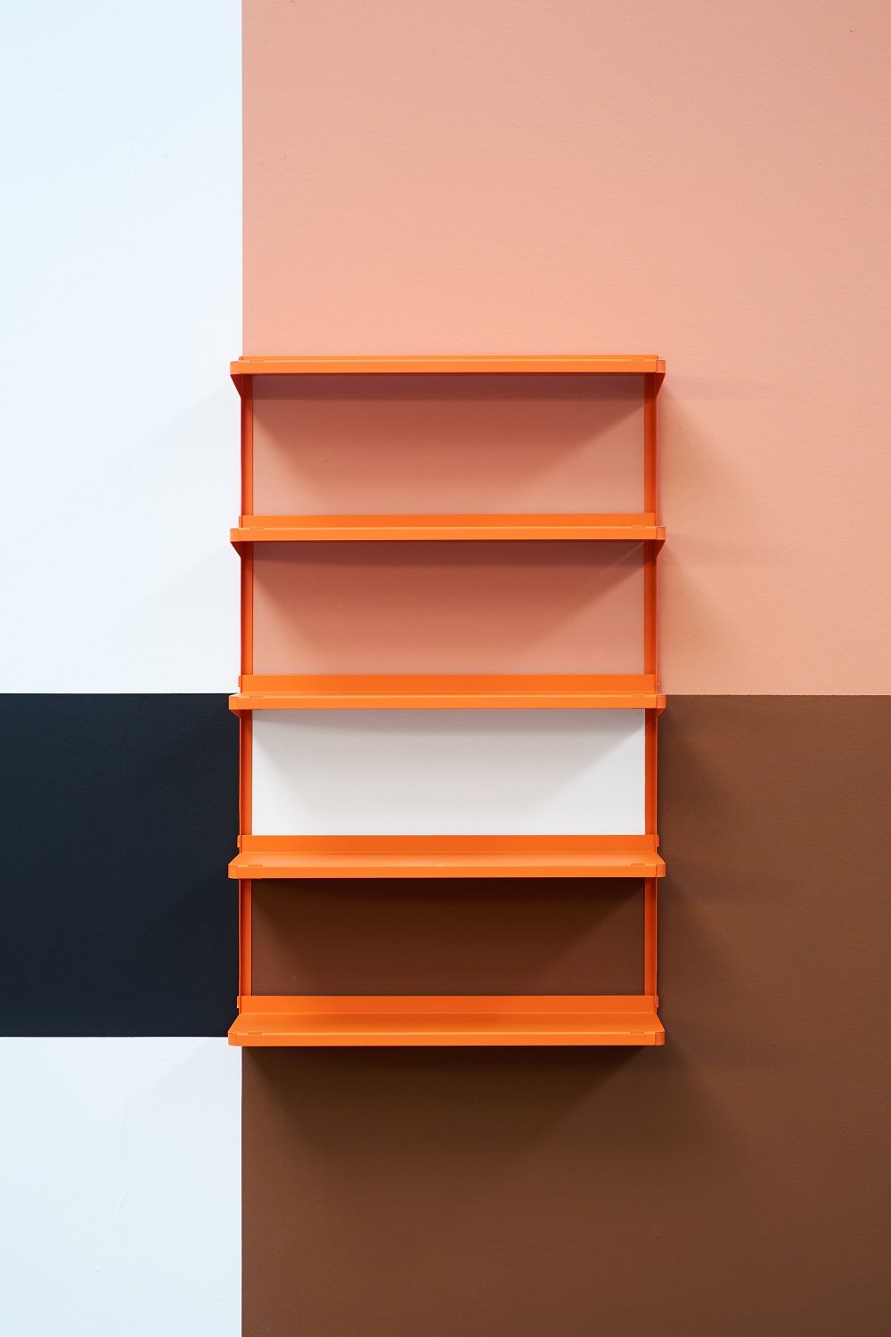 Oranges Click Wandregal von New Tendency vor einer Wand mit Farbquadraten in Weiß, Schwarz, Rosa und Braun.