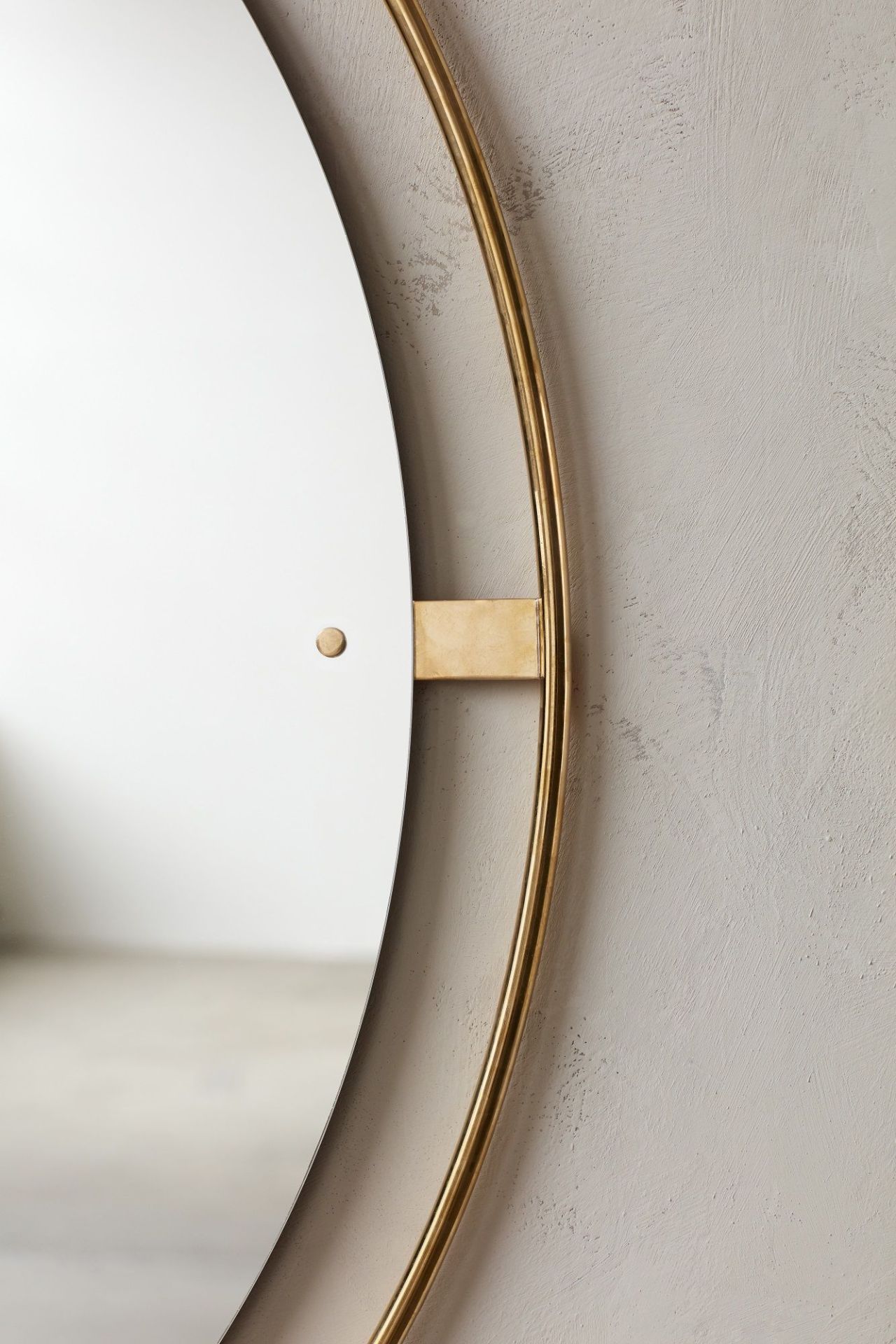 Detailaufnahme des Audo Copenhagen Nimbus Mirror Spiegels mit goldenem Rahmen an einer hellgrauen Wand.