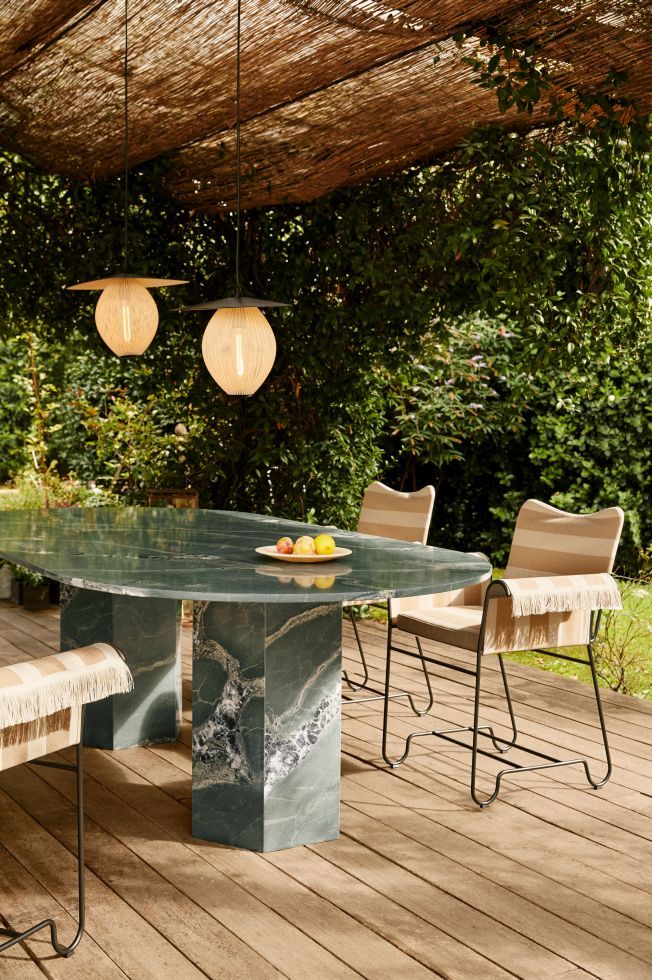 Gubi Epic Outdoor Esstisch Ellipse aus grünem Marmor mit Stühlen und Lampen im Garten.