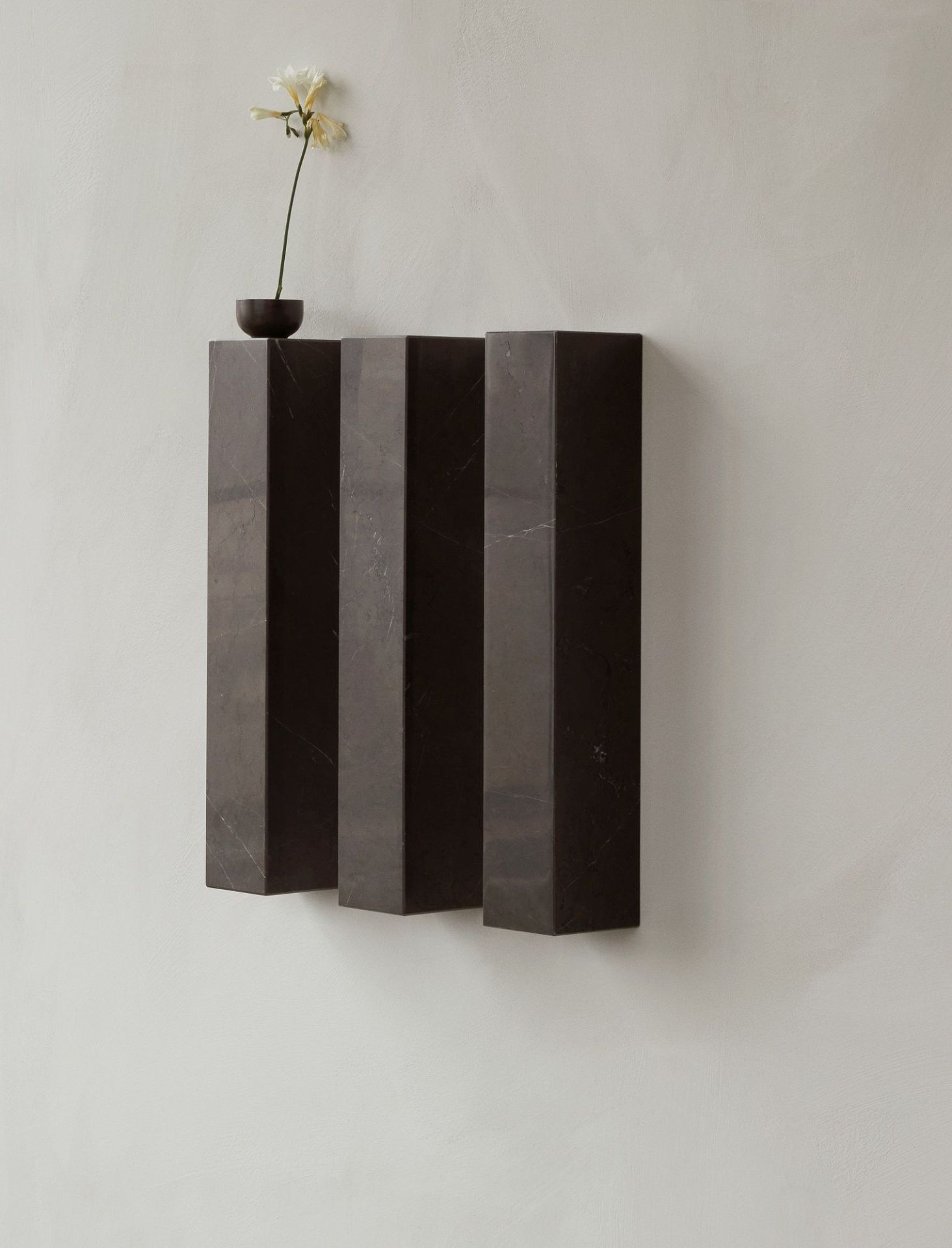 Audo Copenhagen Plinth Shelf Regal aus Marmor mit Blume an der Wand.
