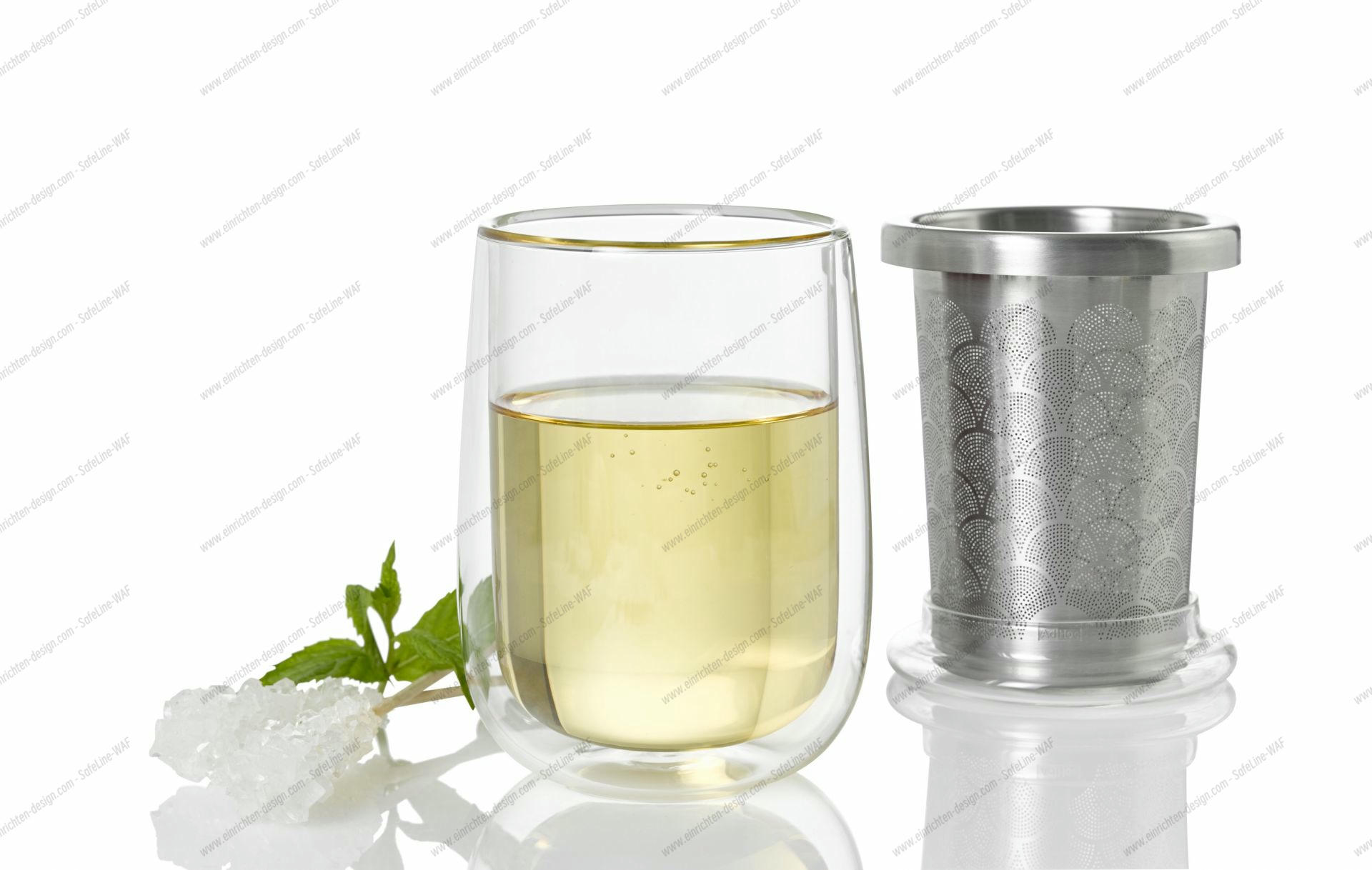 Teeglas mit frischem Tee und Teefilter aus Edelstahl, dazu Kandiszucker und Minze.