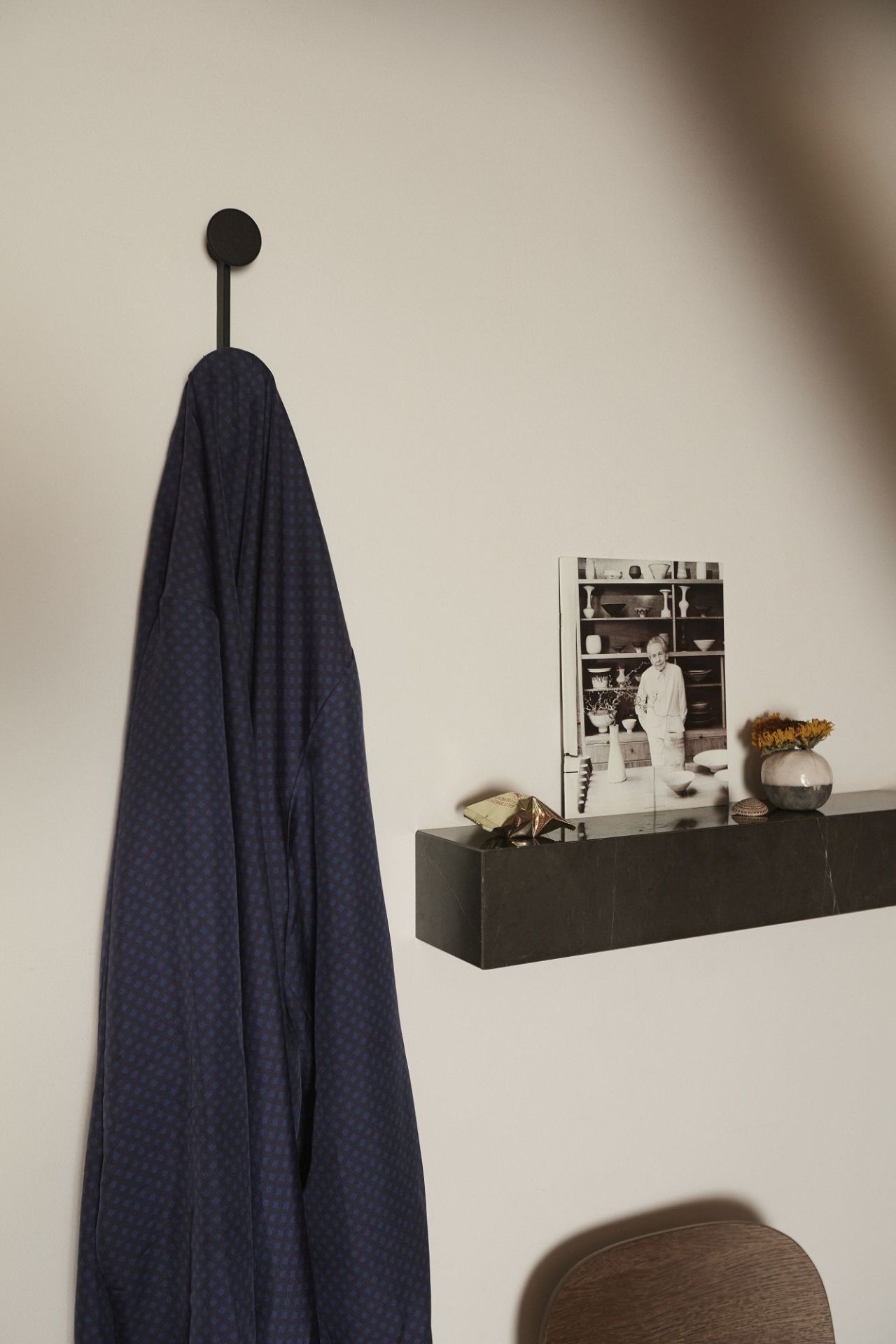 Audo Copenhagen Plinth Shelf Regal aus Marmor mit Dekoration und Jacke an der Wand.