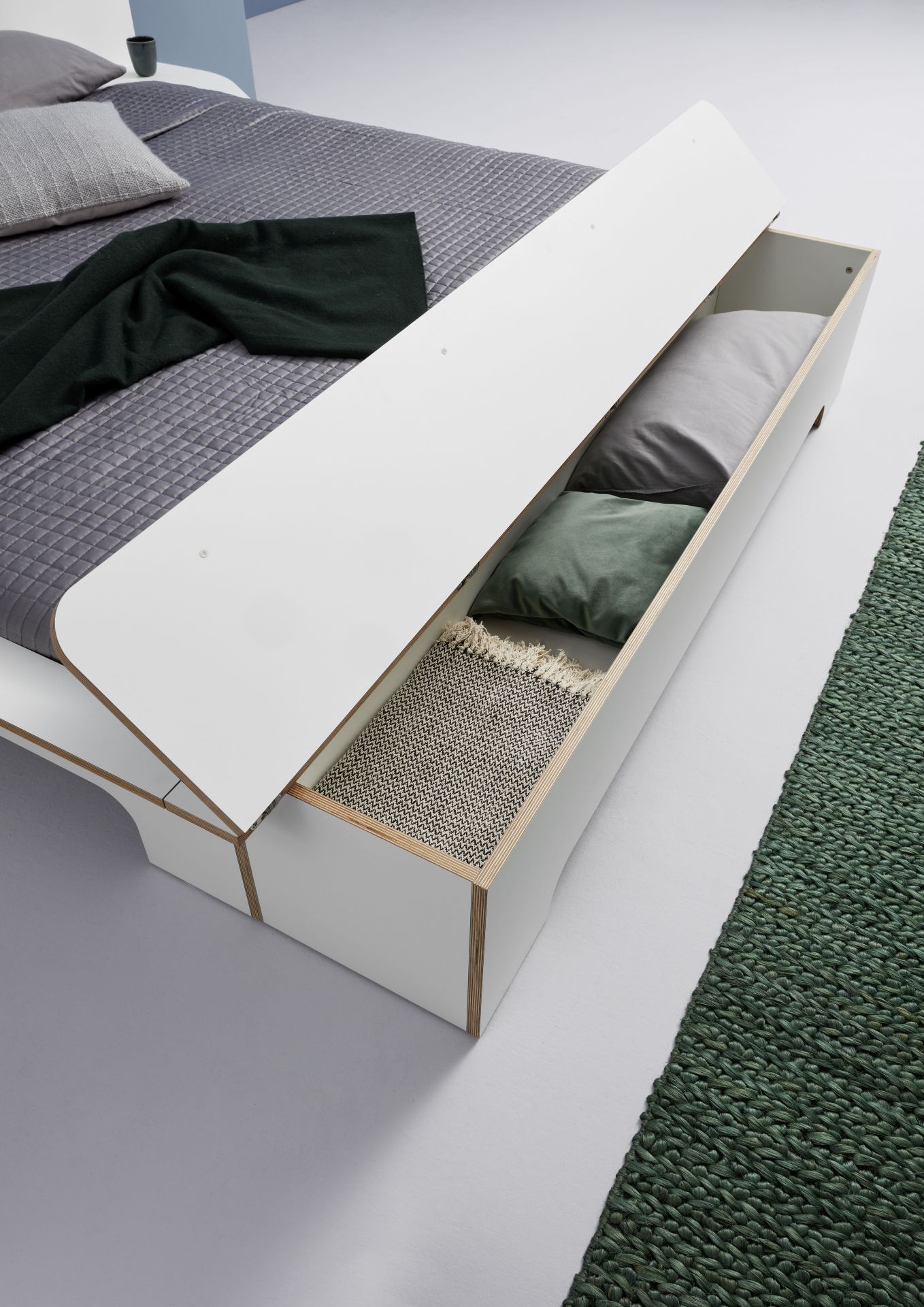 Plane Doppelbett von Müller Möbelwerkstätten mit geöffnetem Bettkasten, der Kissen und eine Decke zeigt.