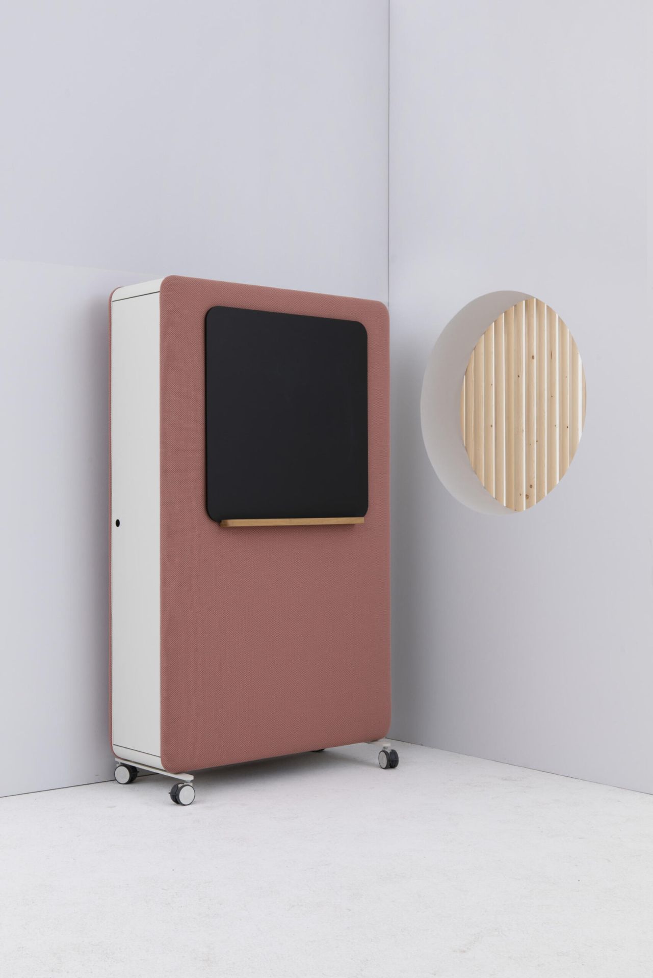 Cascando Pillow Space Akustik Raumteiler in Rosa mit schwarzer Tafel und Rollen vor weißer Wand.