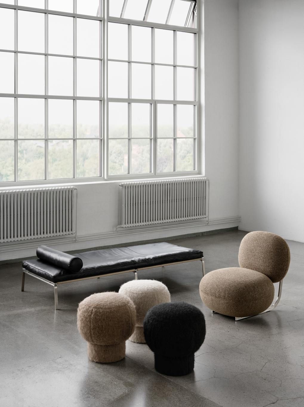 NORR11 Copper Lounge Chair Sessel mit Edelstahlgestell neben Liege und Hockern in modernem Raum.