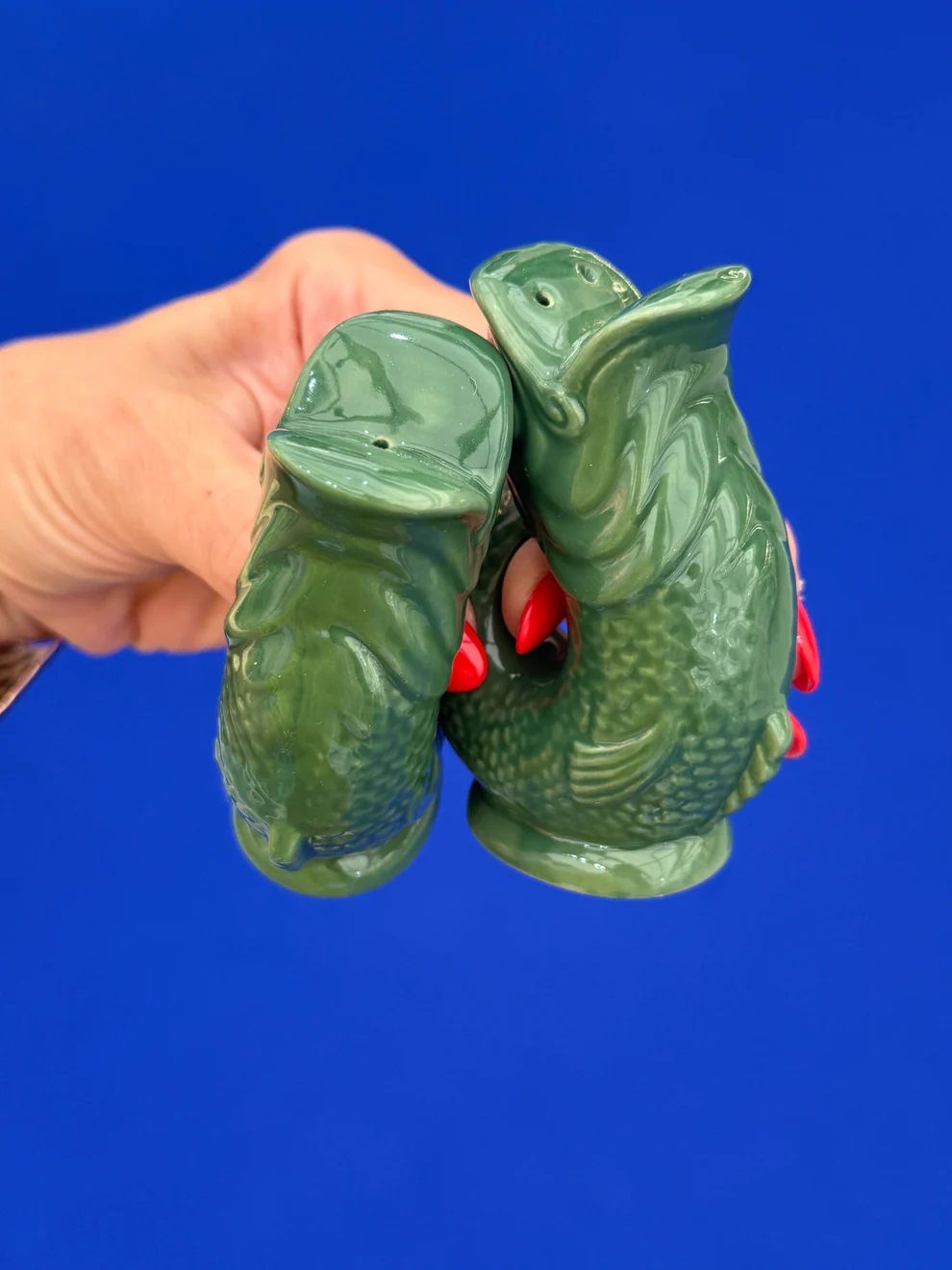 Grüne Gluggle Fisch Salz- und Pfefferstreuer im Detail, gehalten von einer Hand vor blauem Hintergrund.