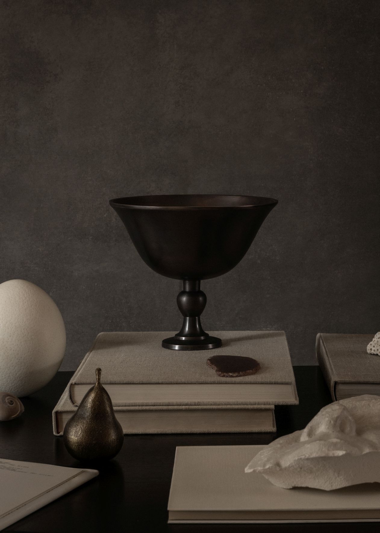 Elegante Audo Copenhagen Pavot Schale aus dunklem Metall auf Bücherstapel, Stillleben mit Deko-Elementen.